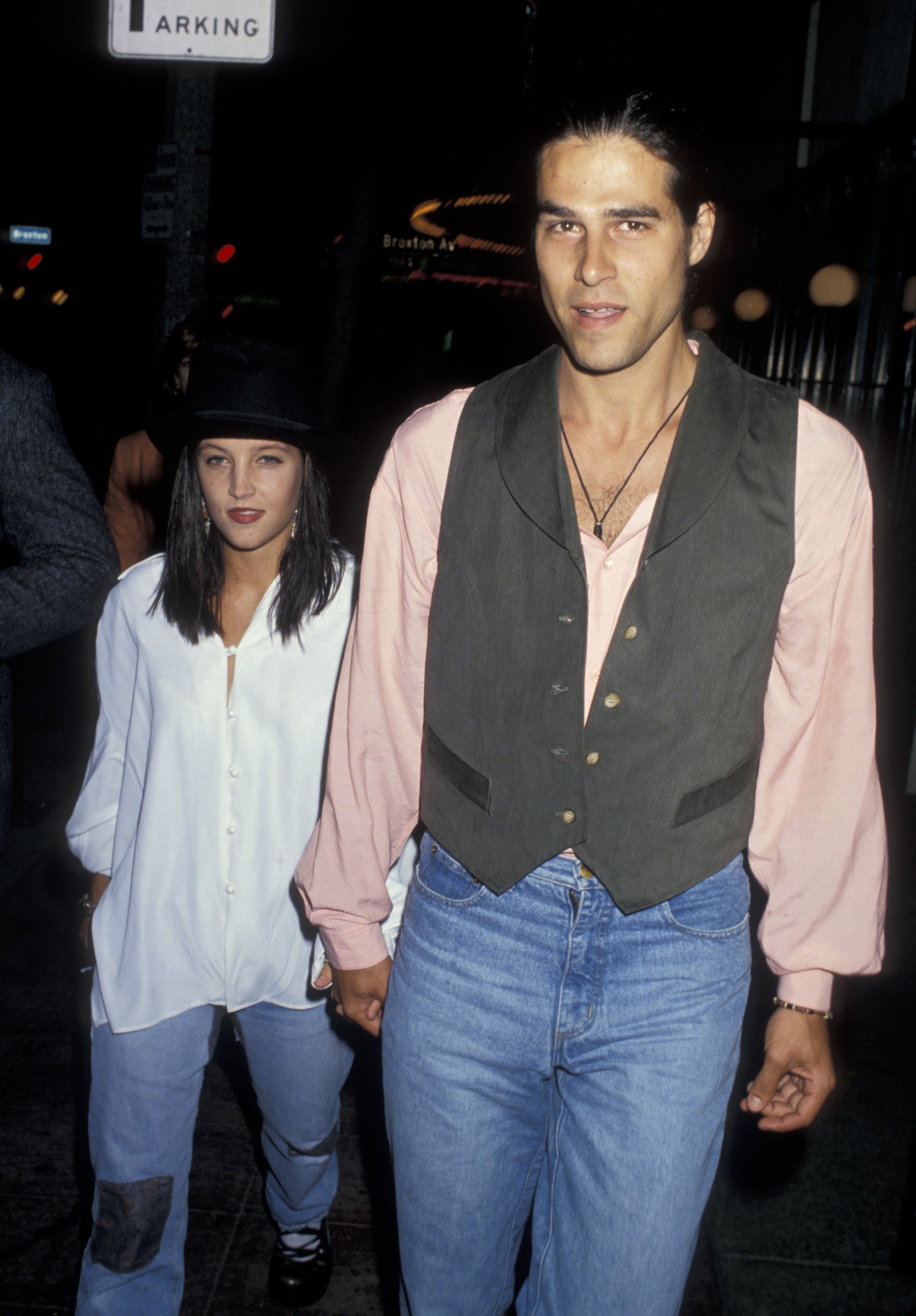 Lisa Marie Presley hält Händchen mit ihrem Ehemann Danny Keough, als sie am 13. Juni 1991. Presley trug eine übergroße weiße Hemdbluse, hellblaue Jeans und einen schwarzen Bowlerhut, während Keough ein blassrosa Hemd mit Kragen unter einer grauen Weste sowie Jeans trug. | Quelle: Getty Images