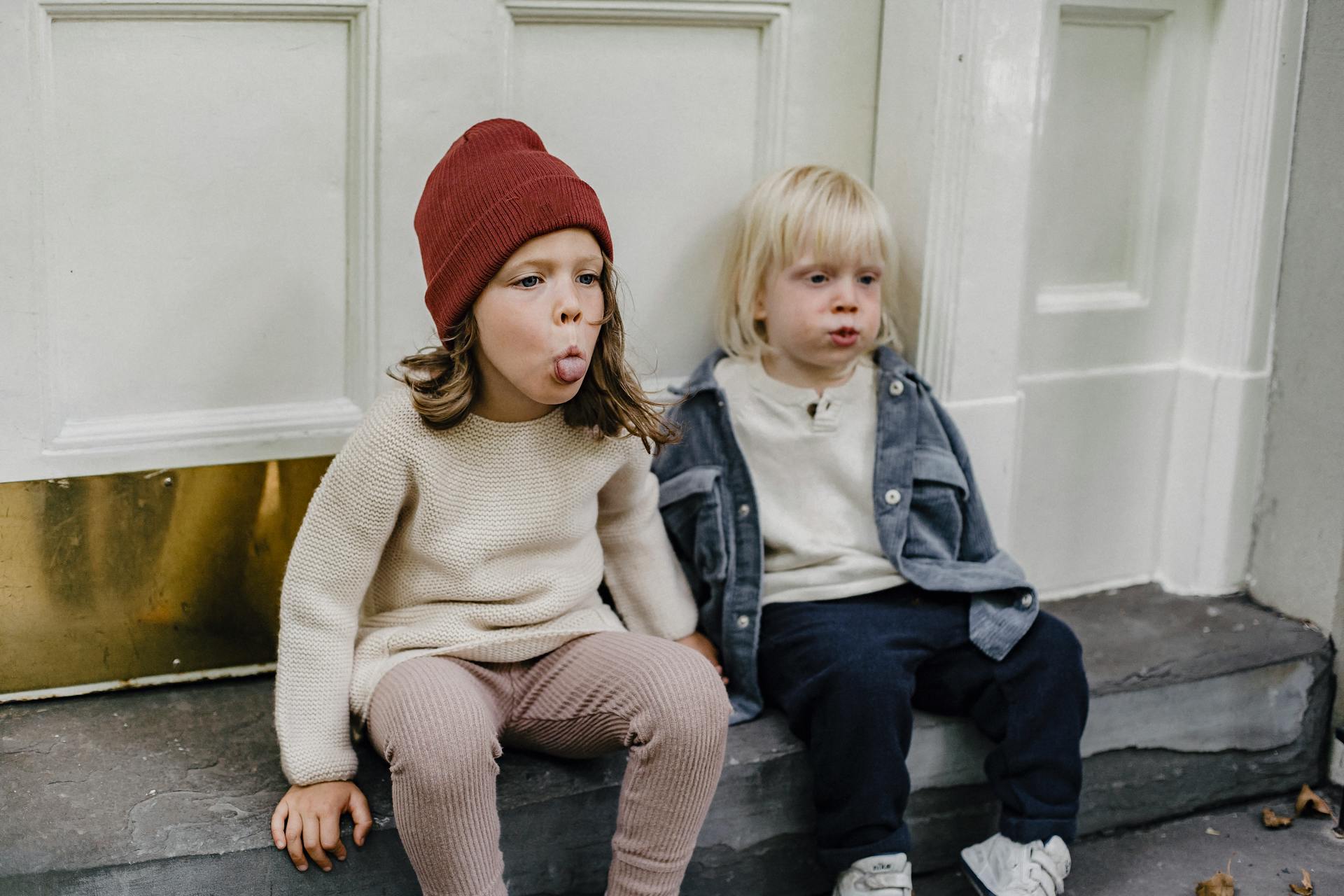 Zwei Kinder sitzen auf der Veranda und machen lustige Grimassen | Quelle: Pexels