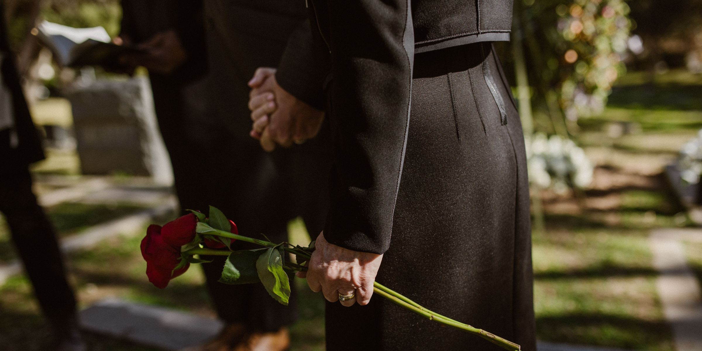 Eine Nahaufnahme einer schwarz gekleideten Frau, die auf einem Friedhof eine rote Rose in der Hand hält | Quelle: Pexels
