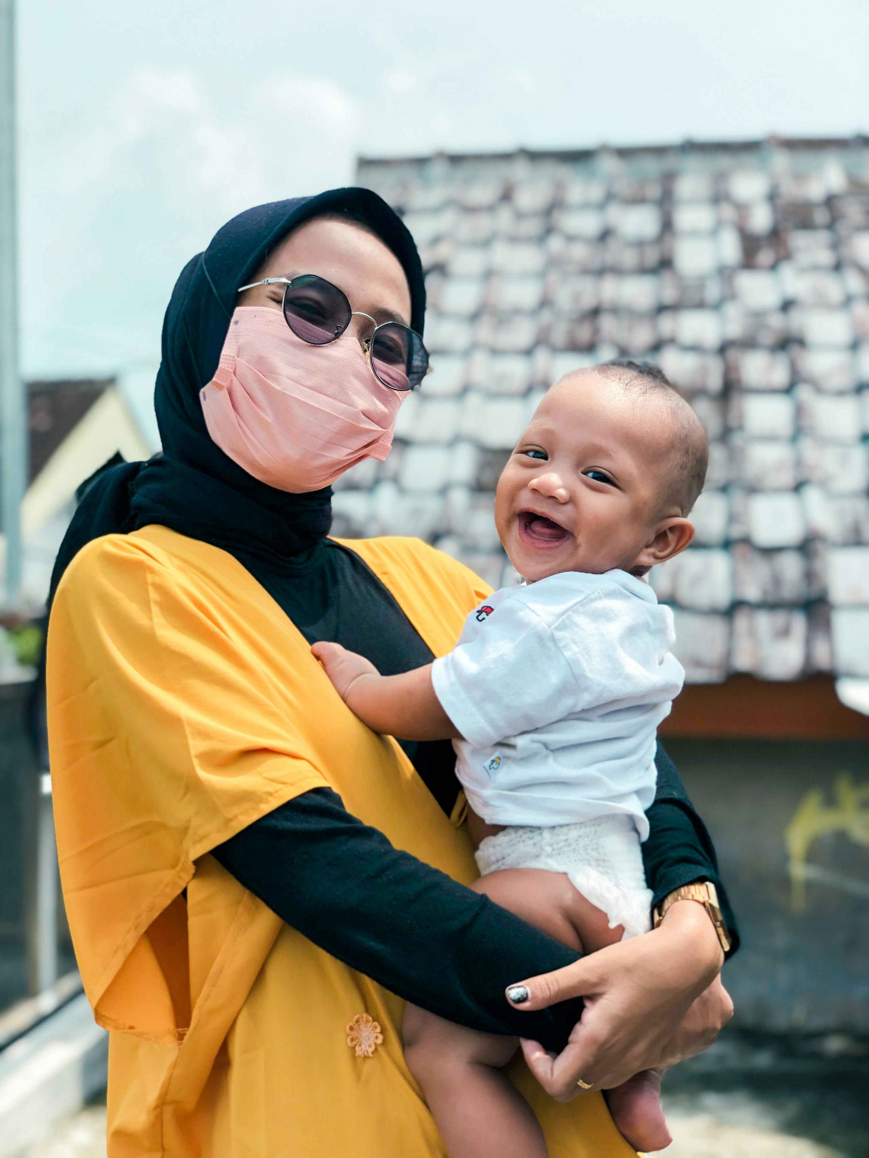 Eine Frau, die eine Maske trägt und ein lächelndes Baby hält | Quelle: Pexels