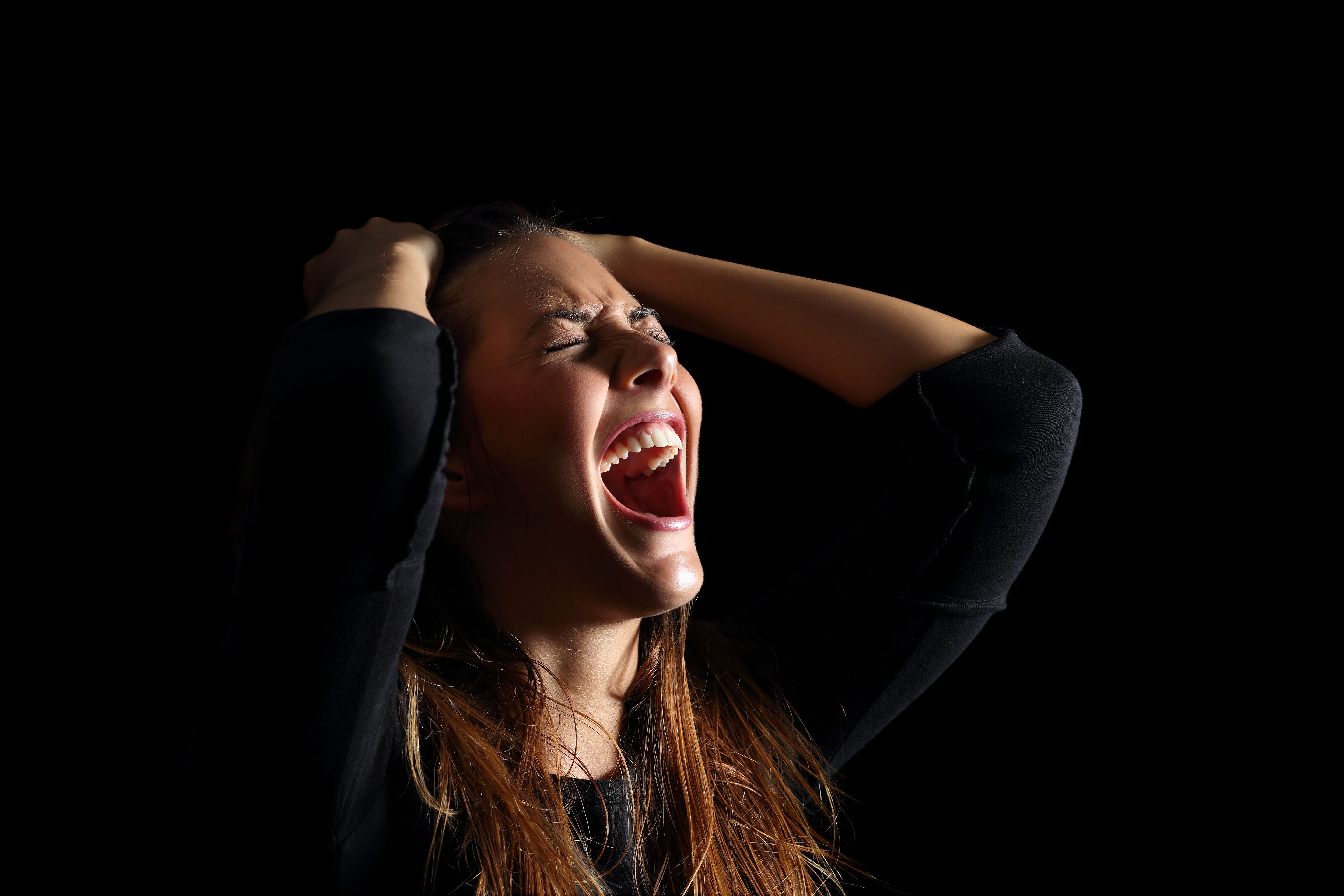 Eine Frau mit geschlossenen Augen und schreiend, während sie ihr Haar hält | Quelle: Getty Images