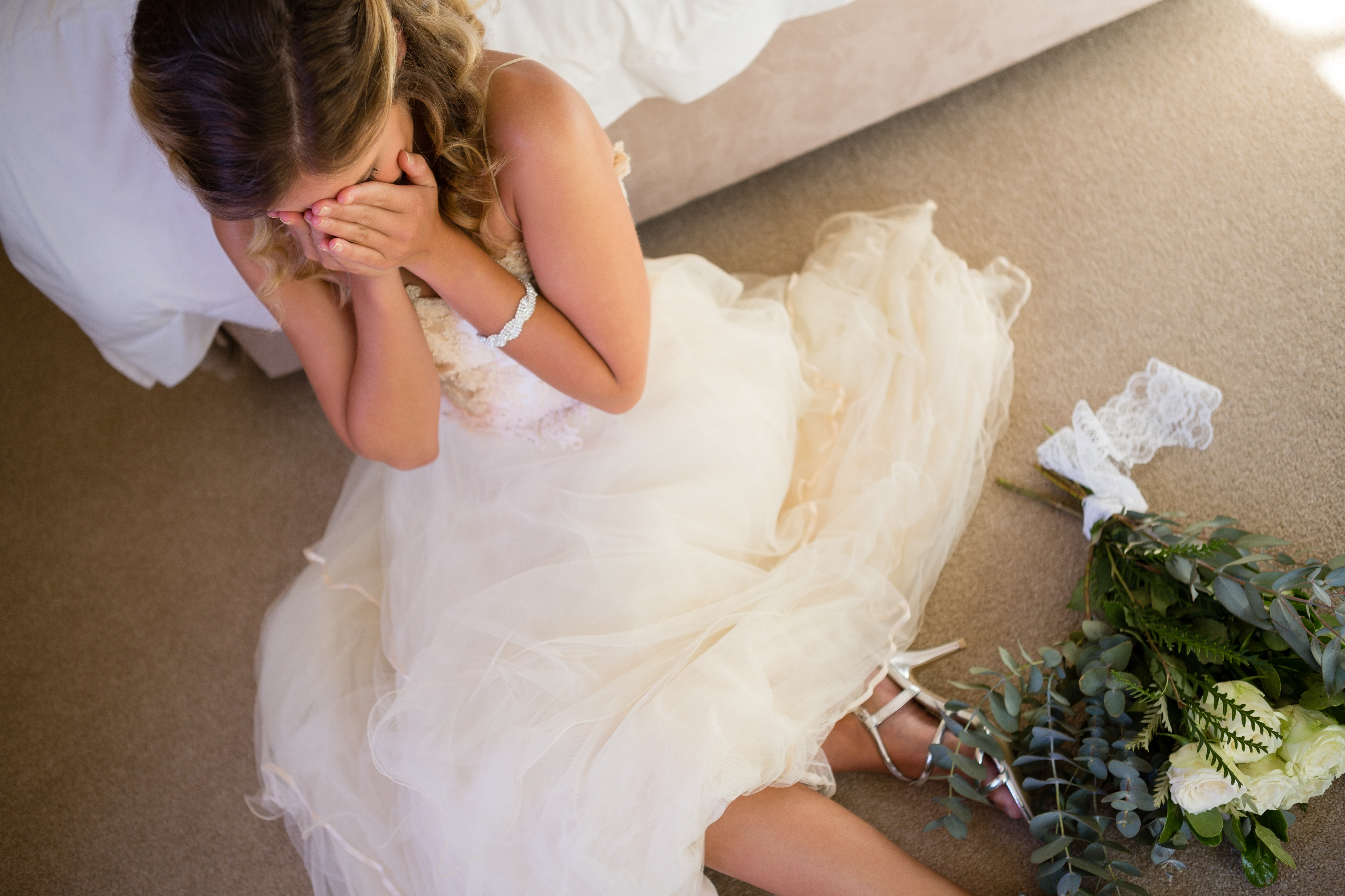 Eine weinende Braut auf dem Boden, während sie sich an ein Bett lehnt | Quelle: Shutterstock