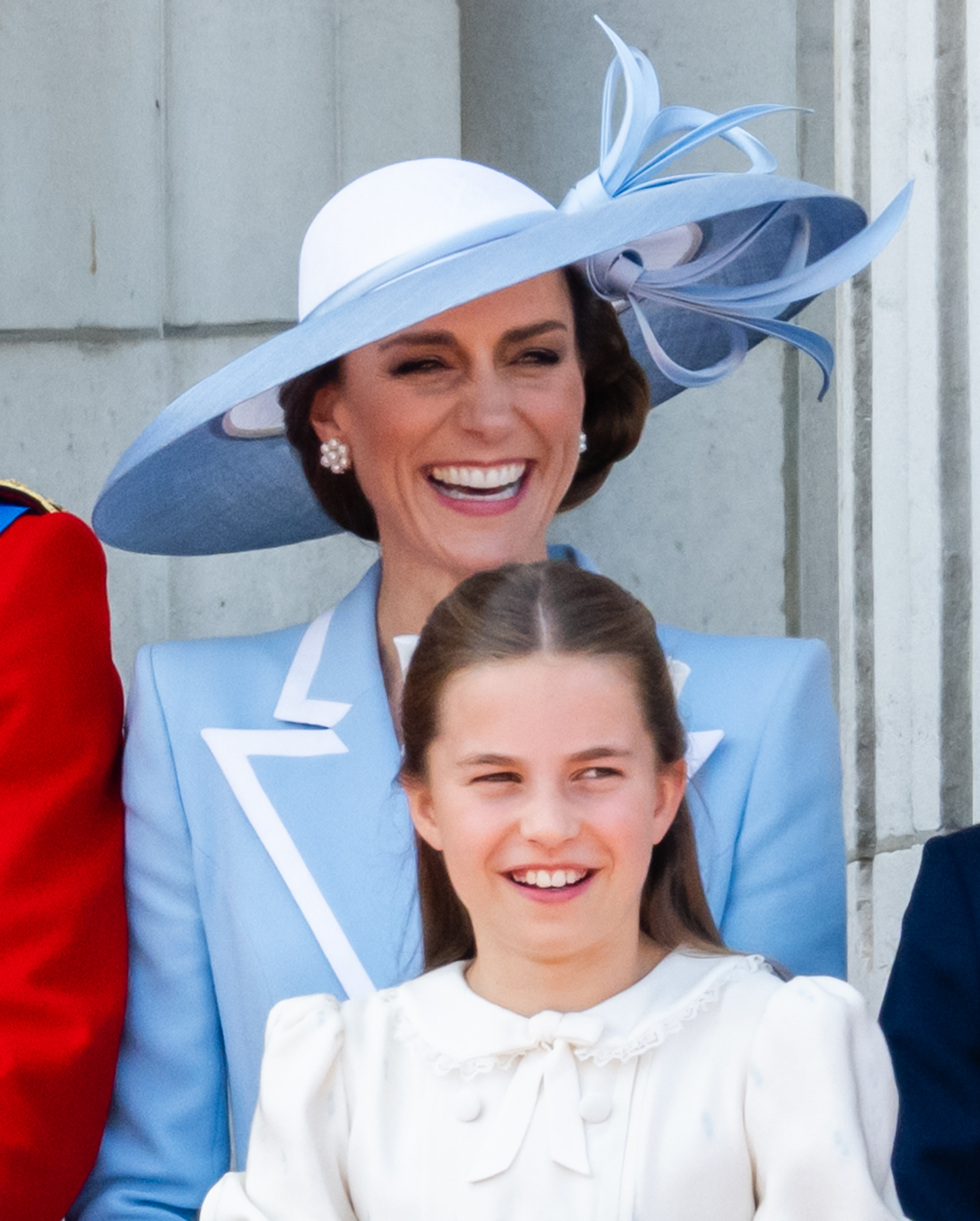 Prinzessin Charlotte von Wales und Catherine, Prinzessin von Wales, lachen fröhlich gemeinsam auf dem Balkon des Buckingham Palace, während sie am 13. Juni 2026 in London, England, den Überflug der RAF beim „Trooping the Colour“ verfolgen. Charlotte strahlt in einem elfenbeinfarbenen Kleid mit gerüschtem Spitzenkragen und einer Schleife am Ausschnitt und steht vor Catherine, die ein puderblaues, tailliertes Mantelkleid mit knackig weißen Reversakzenten, Perlenohrringen und einem architektonisch gestalteten Philip-Treacy-Hut trägt, der mit geformten Schleifen verziert ist. | Quelle: Getty Images