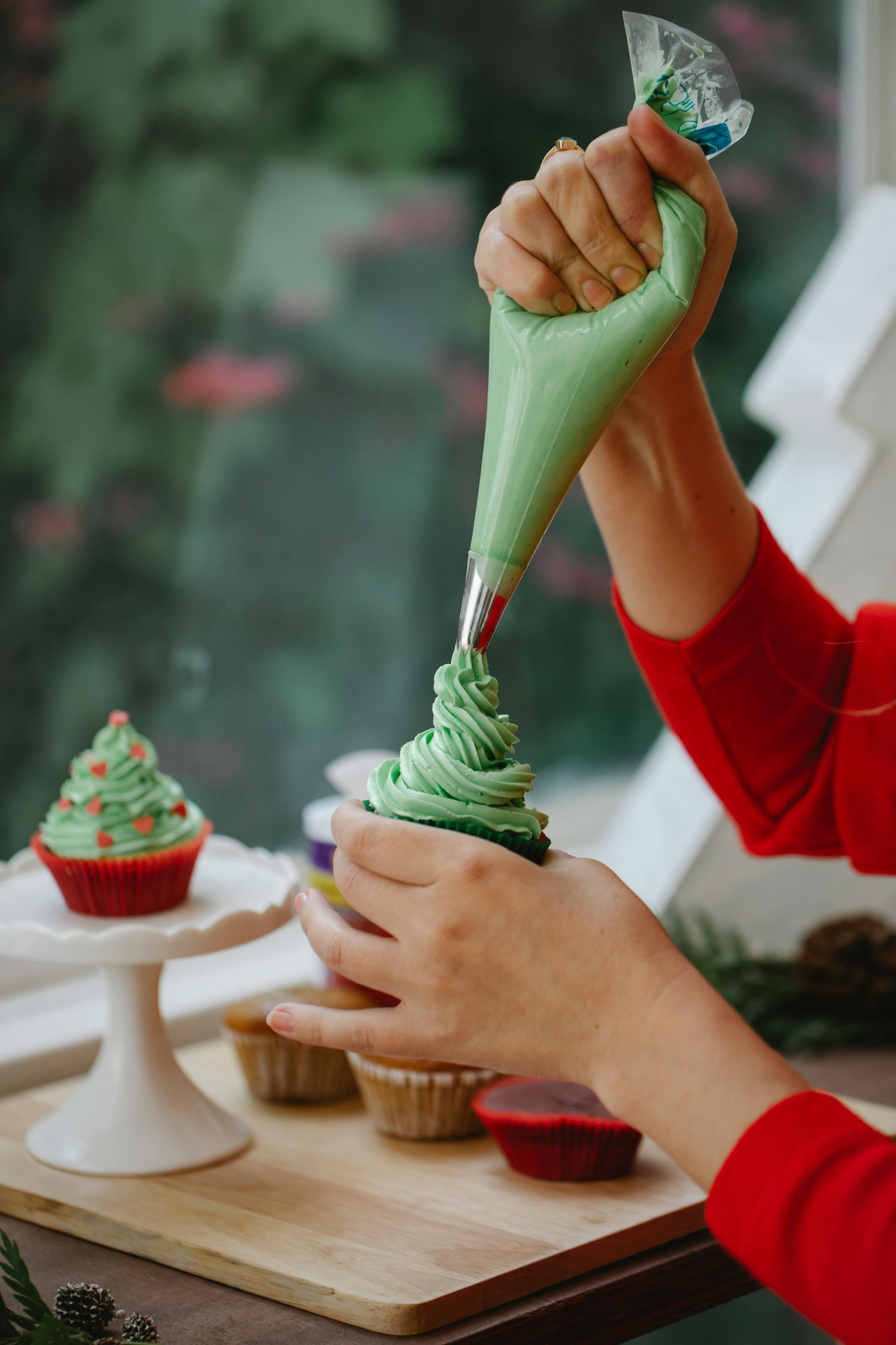 Eine Nahaufnahme einer Frau, die einen selbst gebackenen Cupcake mit Sahne verziert | Quelle: Pexels