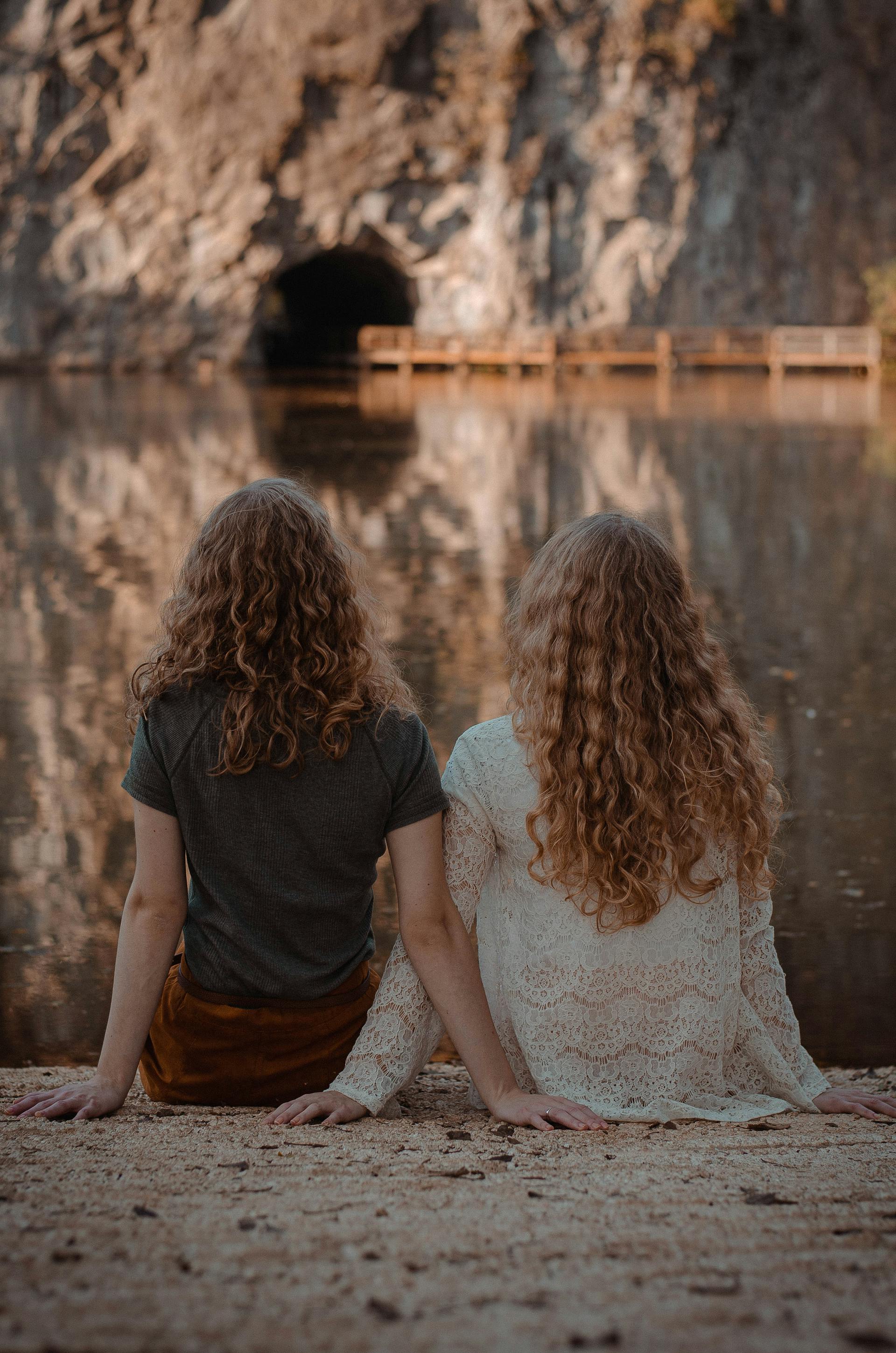 Zwei Frauen sitzen auf dem Boden vor einem Gewässer | Quelle: Pexels