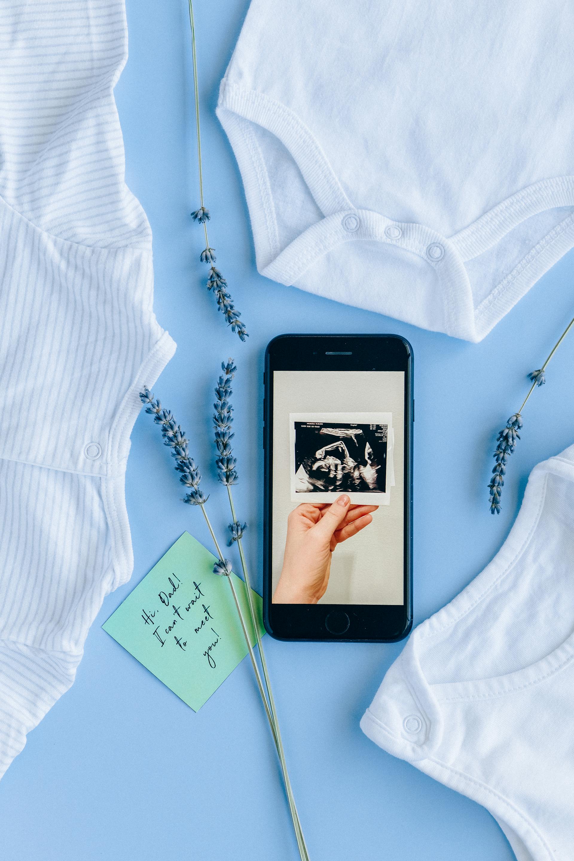 Ein Ultraschallbild auf einem Telefondisplay neben Babykleidung | Quelle: Pexels