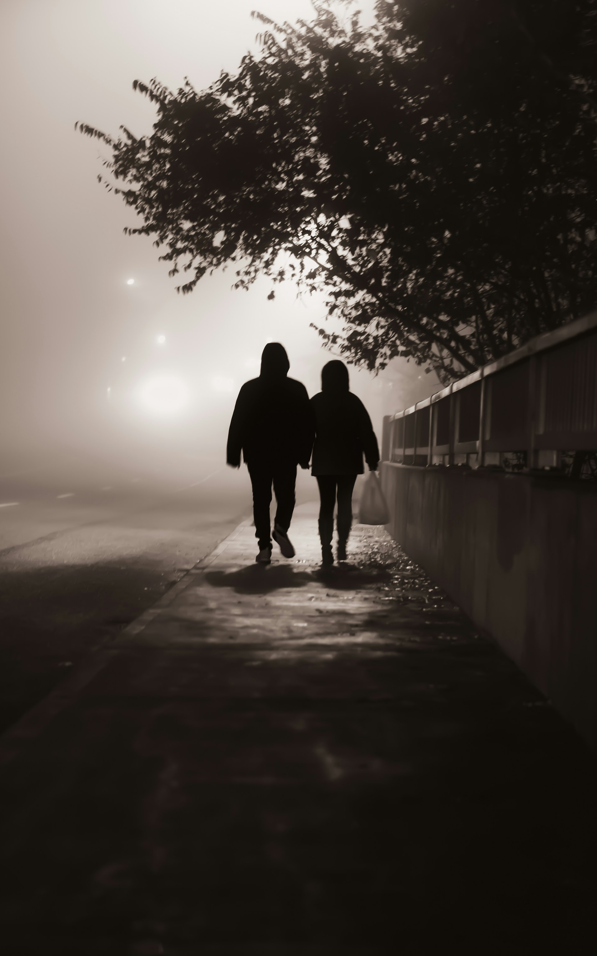 Ein Paar, das an einem nebligen Abend auf dem Bürgersteig spazieren geht | Quelle: Unsplash