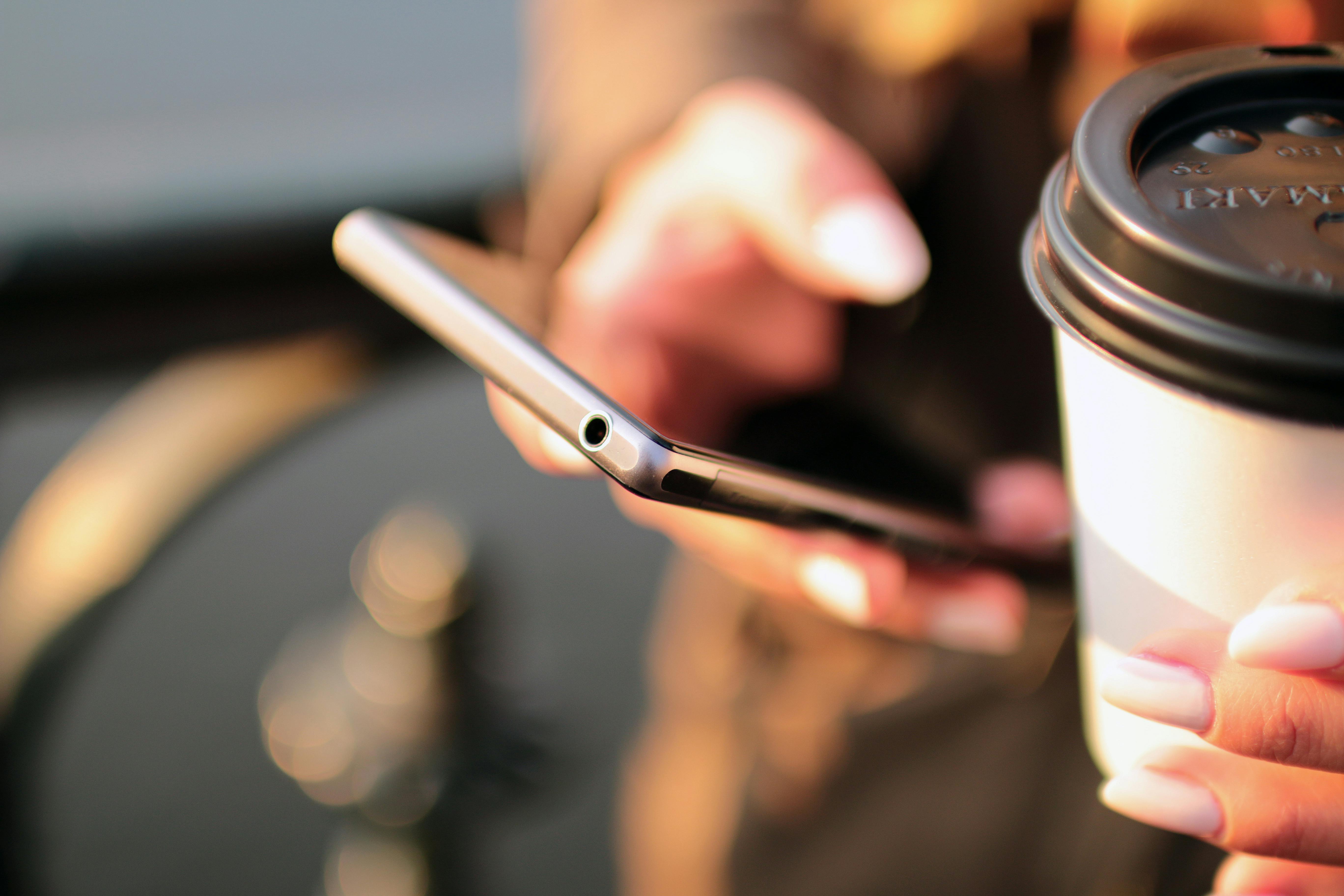 Nur zu Illustrationszwecken. Frau liest Text auf ihrem Telefon, während sie Kaffee trinkt | Quelle: Pexels