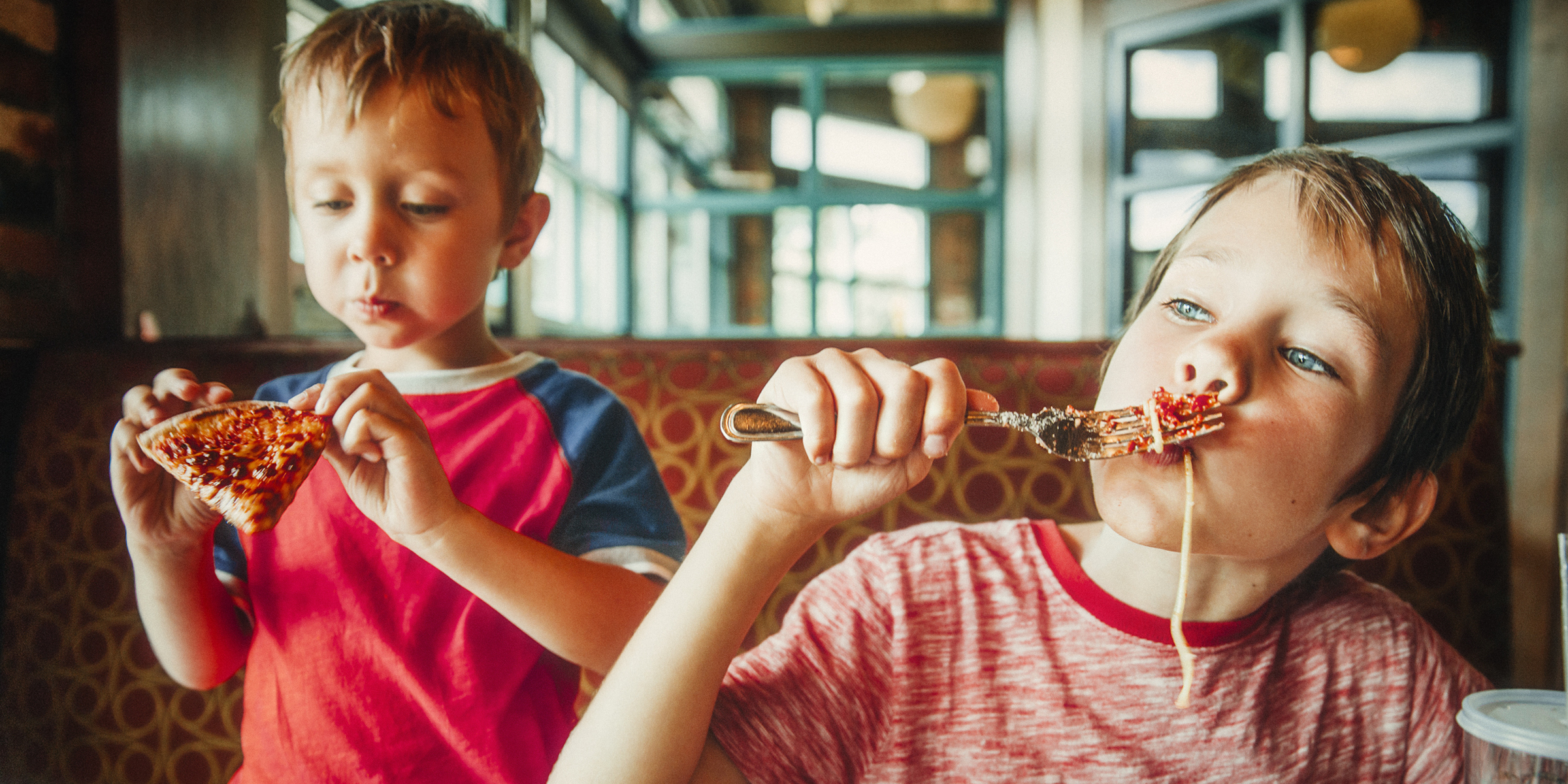 Zwei Kinder genießen Pizza und Pasta in einem Restaurant | Quelle: Shutterstock