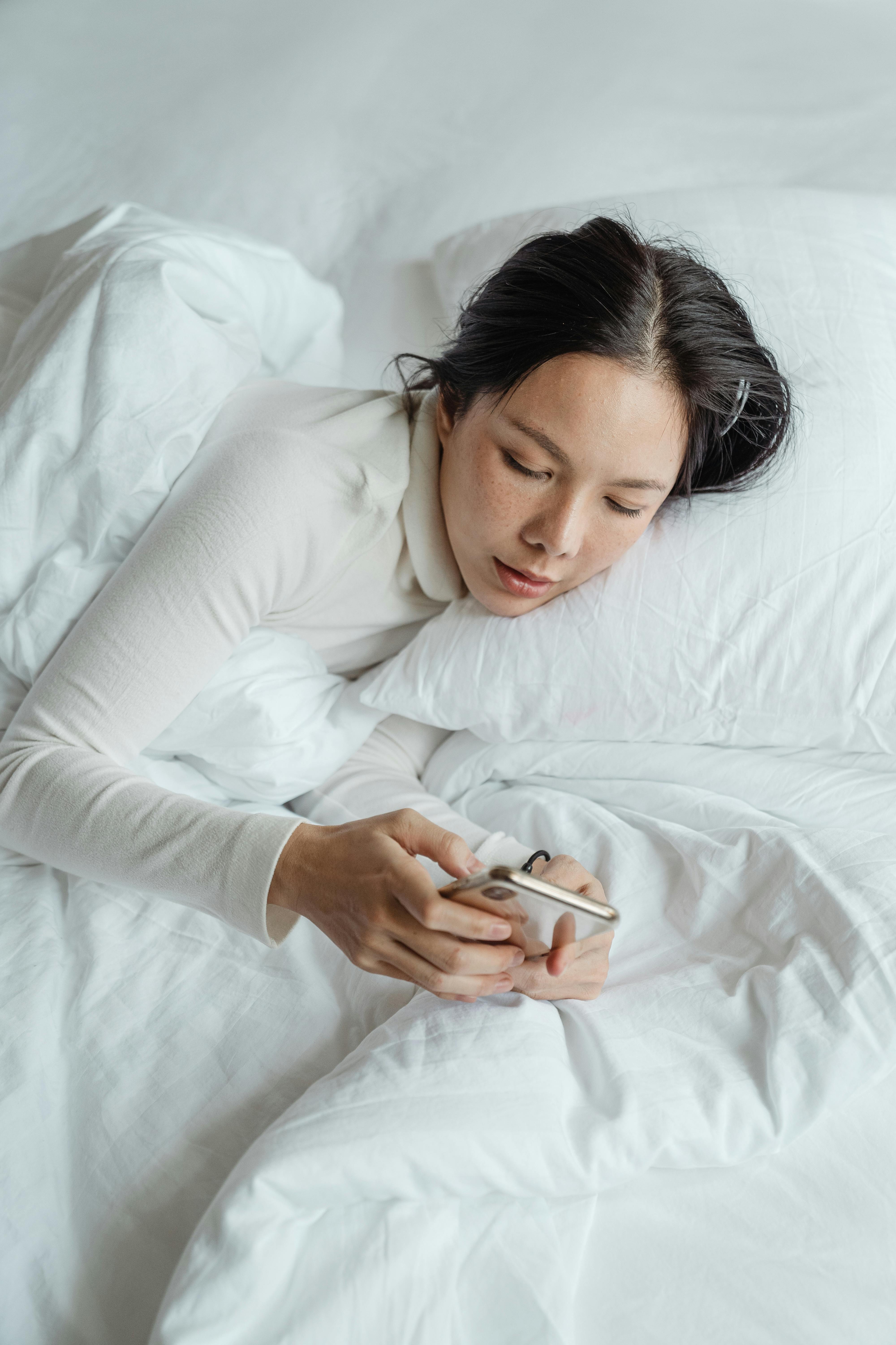 Eine Frau schreibt eine SMS auf ihrem Handy, während sie im Bett liegt | Quelle: Pexels