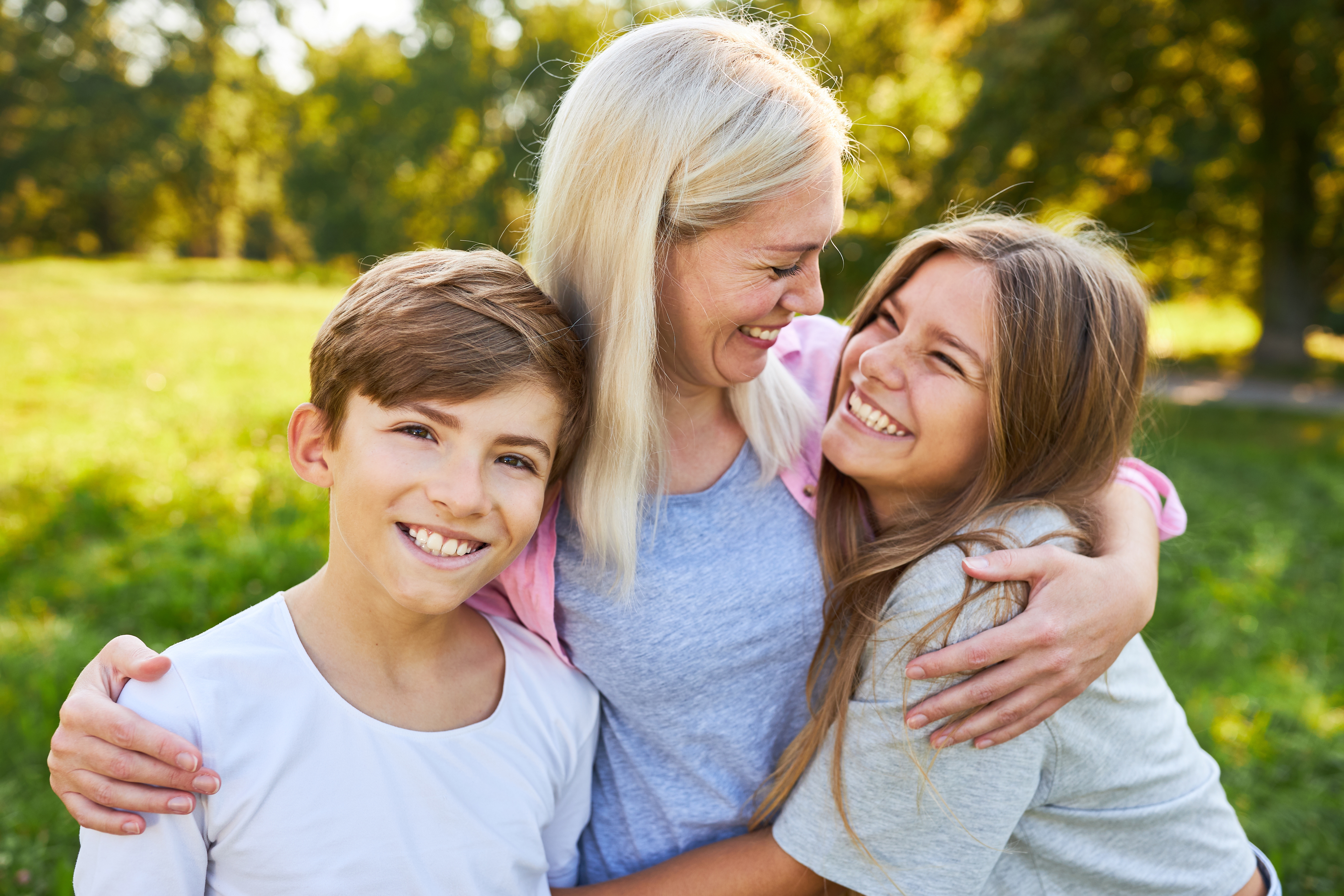 Eine glückliche Mutter, die ihre beiden Kinder im Freien umarmt | Quelle: Shutterstock