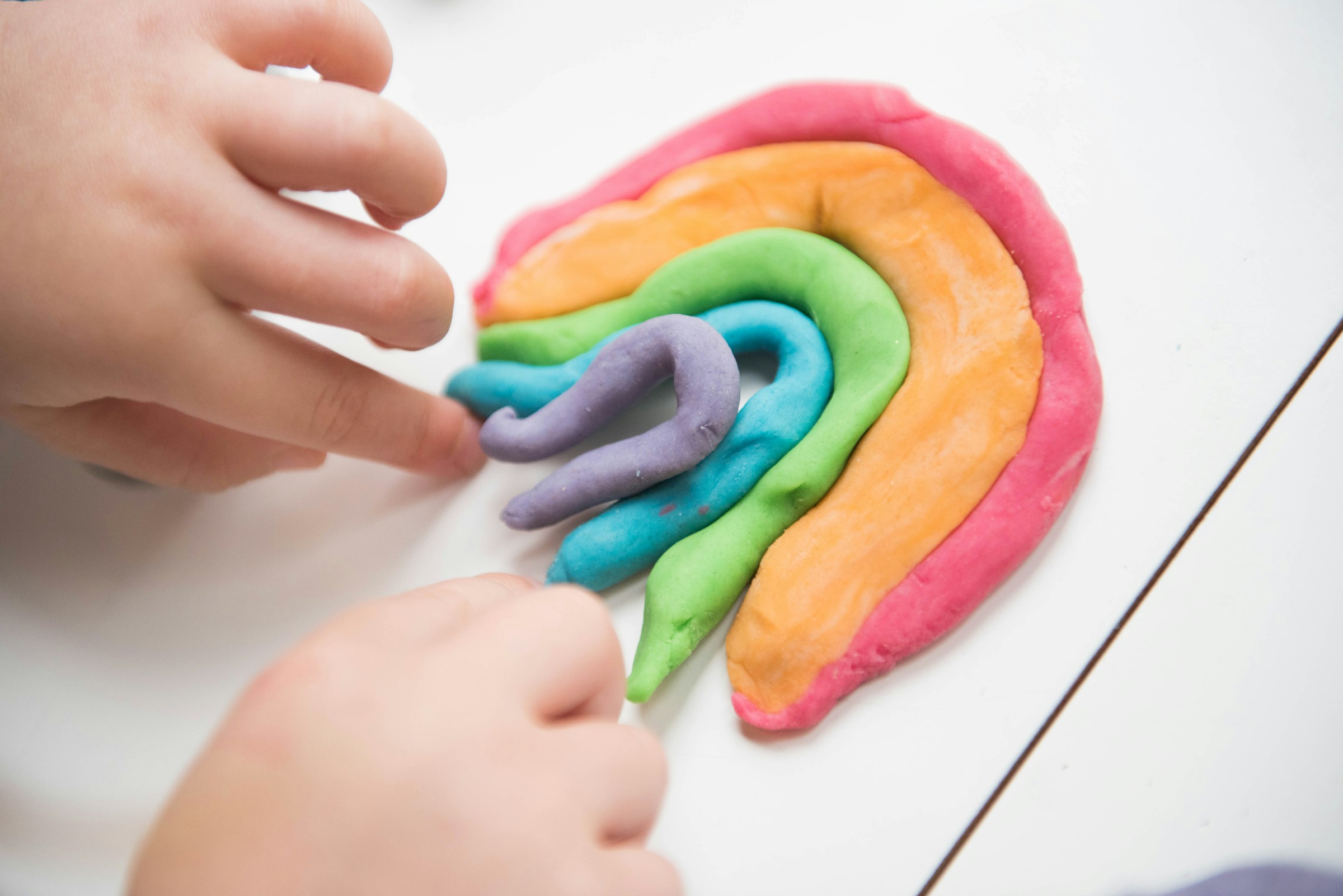 Nahaufnahme eines Kindes, das mit bunten Play-Doh-Streifen spielt | Quelle: Unsplash