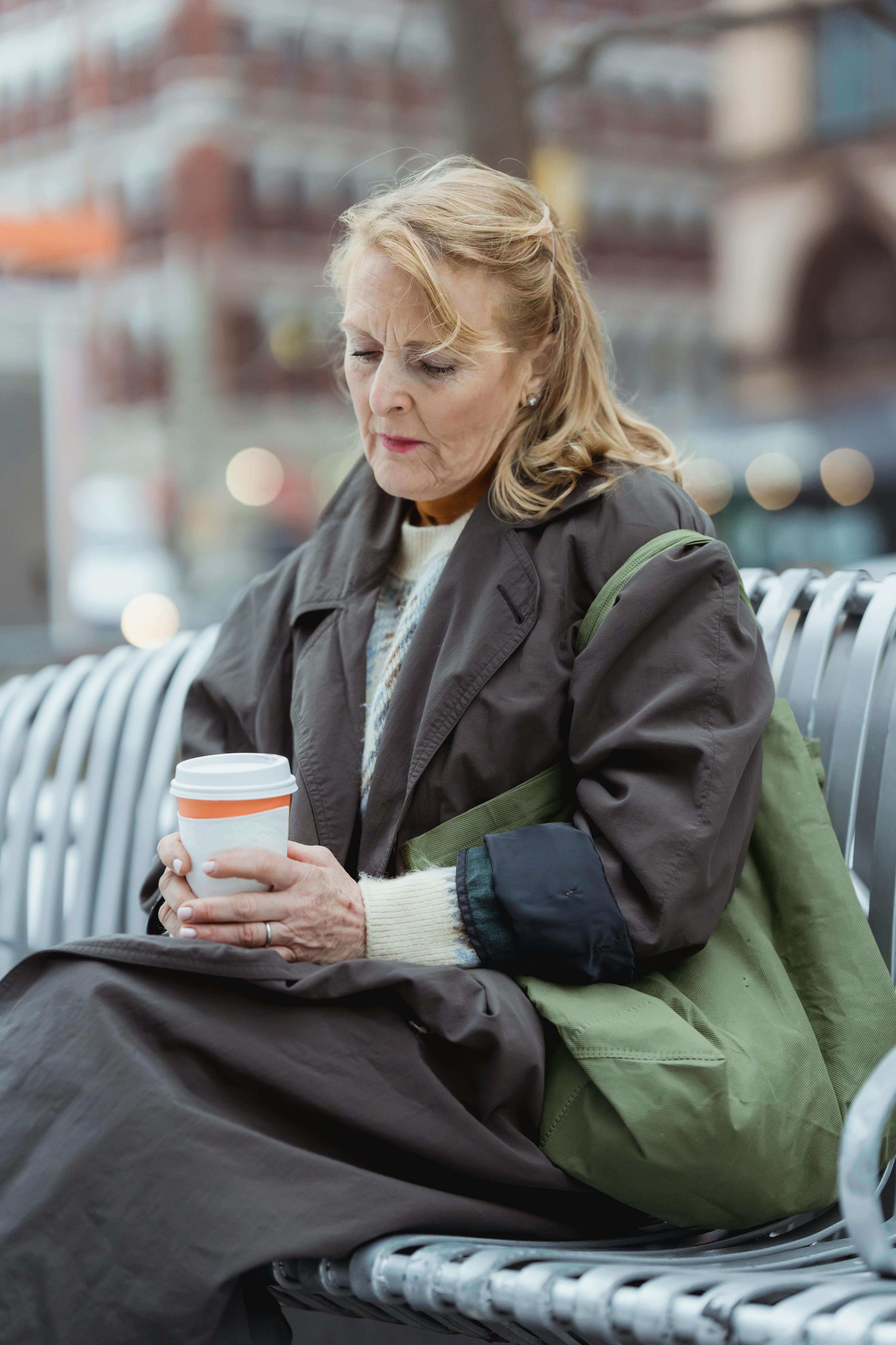 Eine aufgebrachte ältere Frau mit einem Getränk in der Hand, während sie auf einer Bank im Freien sitzt | Quelle: Pexels