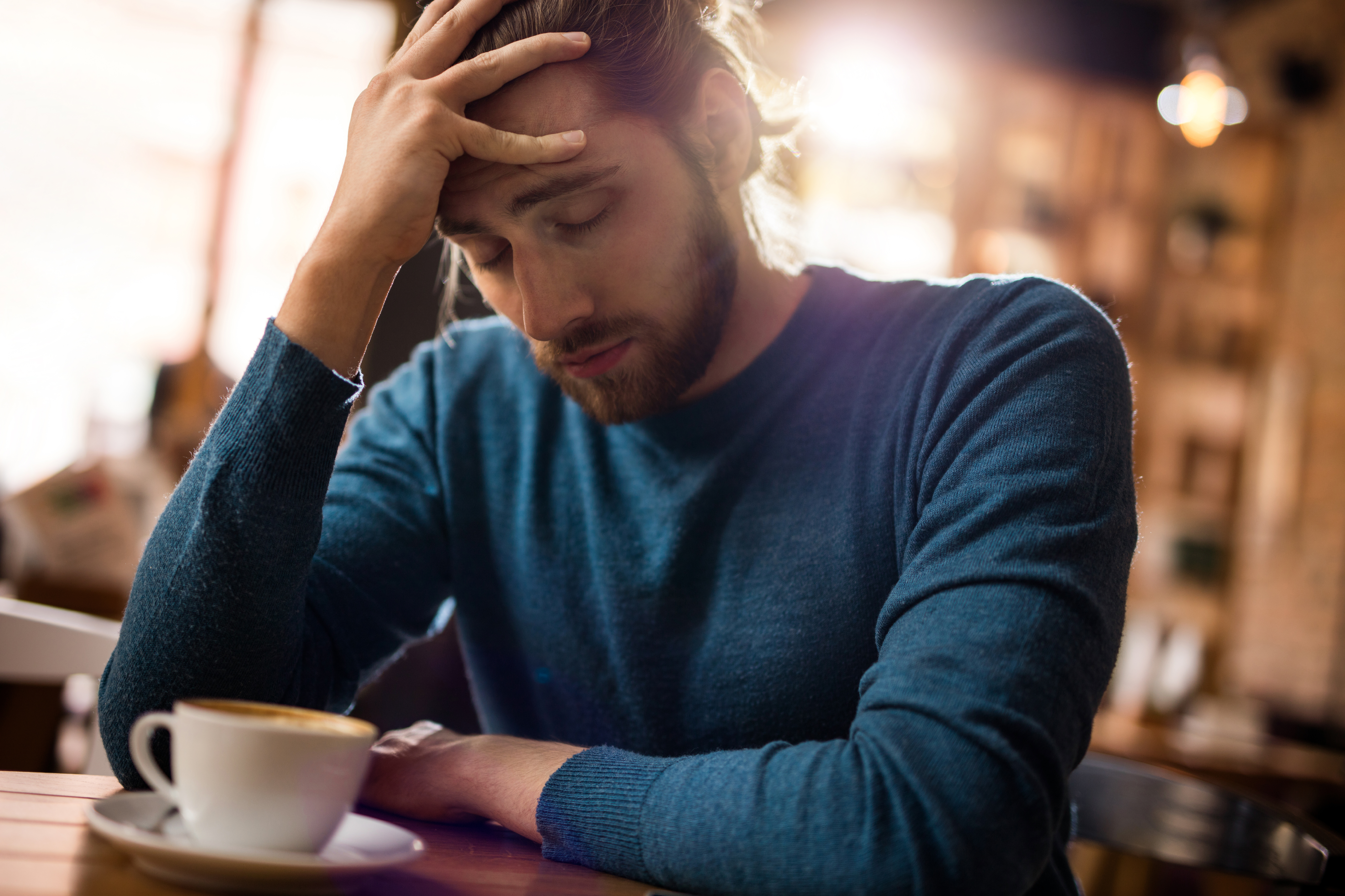 Gestresster Mann, der sich in einem Café den Kopf vor Schmerzen hält | Quelle: Getty Images