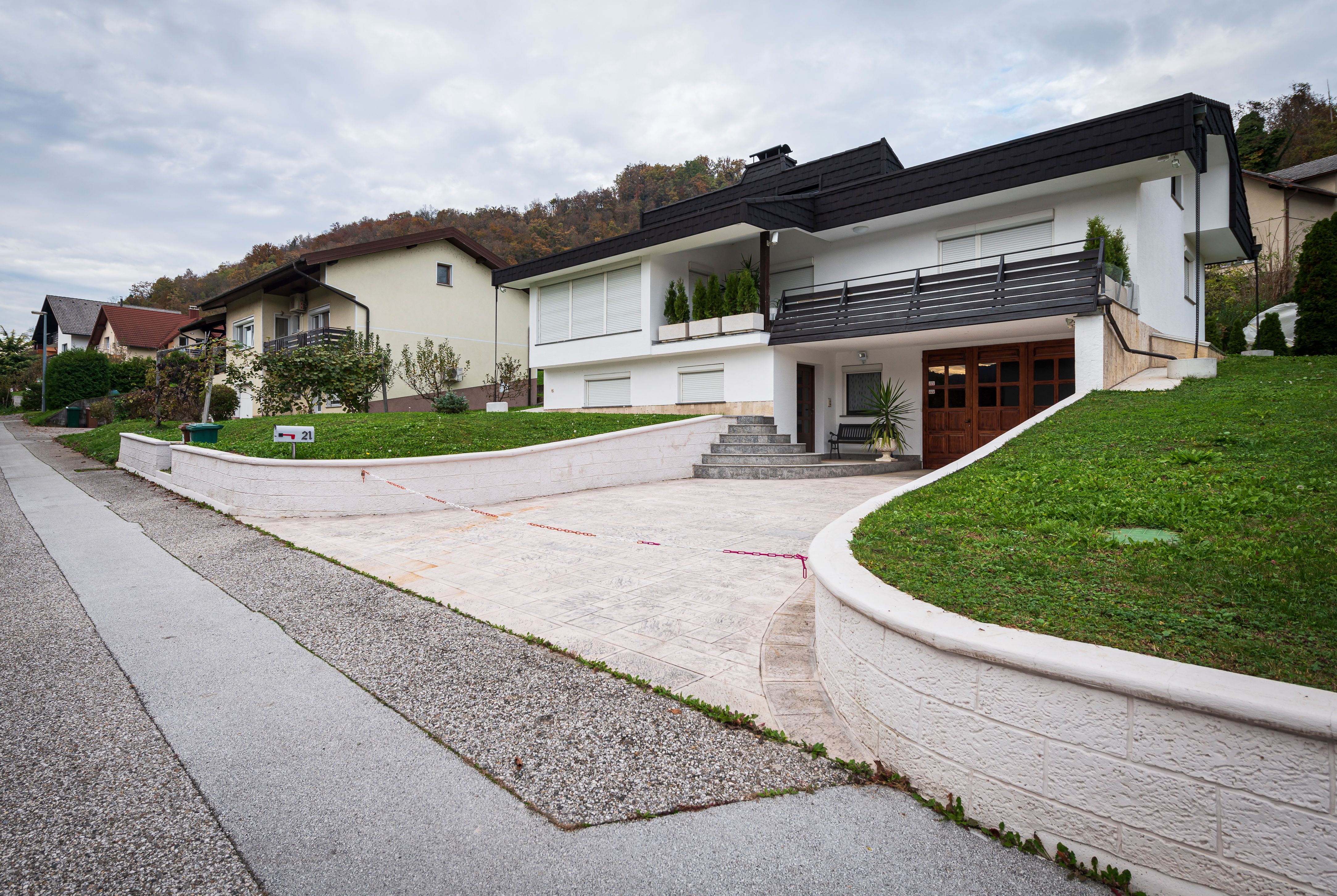 Eine schräg aufgenommene Straßenansicht zeigt das am Hang gelegene Einfamilienhaus in Sevnica, Slowenien, in dem Melania Trump in ihrer Jugend lebte, aufgenommen am 30. Oktober 2020. Das schlichte, schwarz-weiße Haus mit versetzten Ebenen liegt auf einem erhöhten, grünen Rasen an einer ruhigen Wohnstraße und verfügt über eine breite, gepflasterte Auffahrt, eine Außentreppe aus Stein und eine Terrasse mit dunklem Geländer. | Quelle: Getty Images