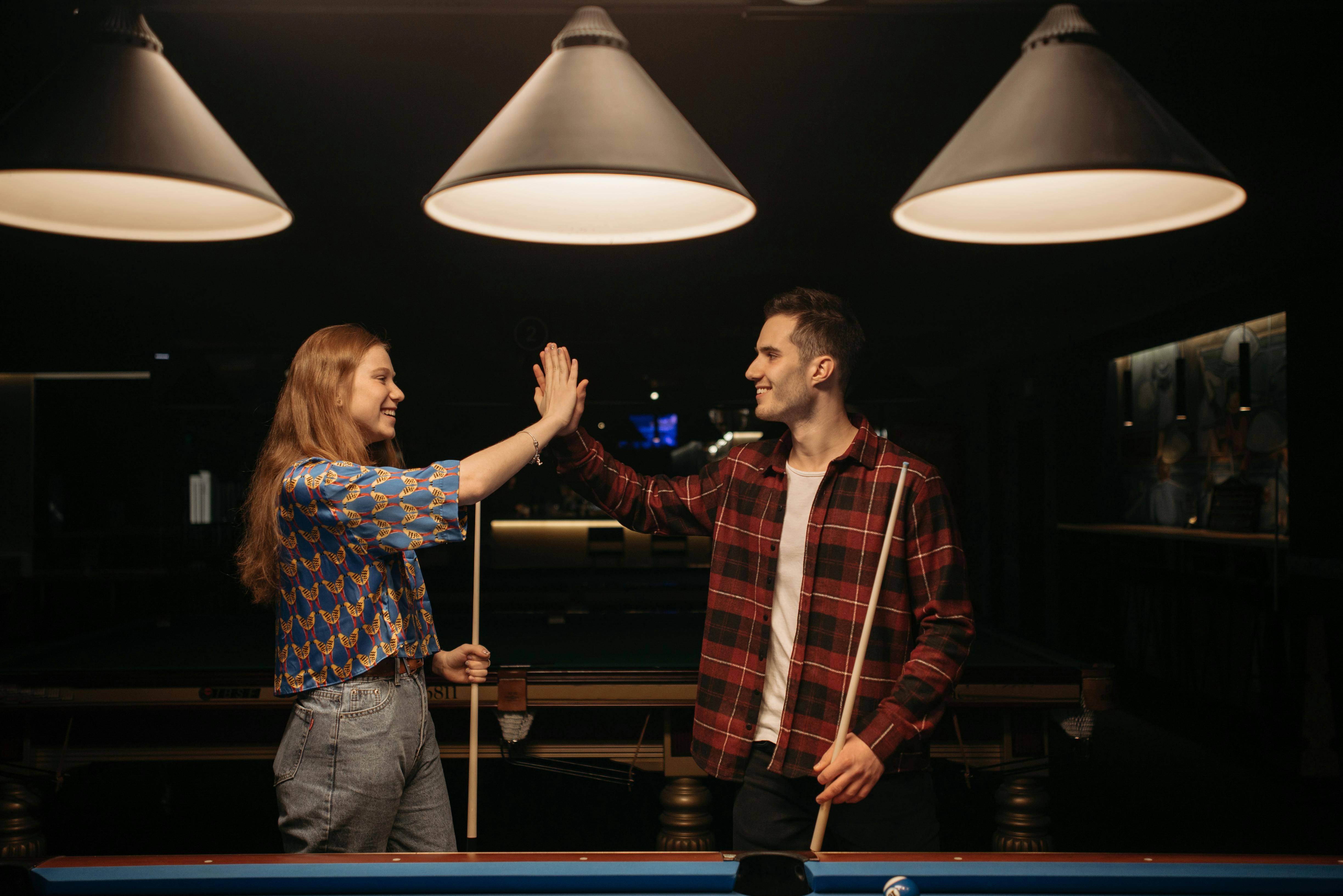 Ein Mann und eine Frau, die sich in der Nähe eines Billardtisches ein High-Five geben | Quelle: Pexels