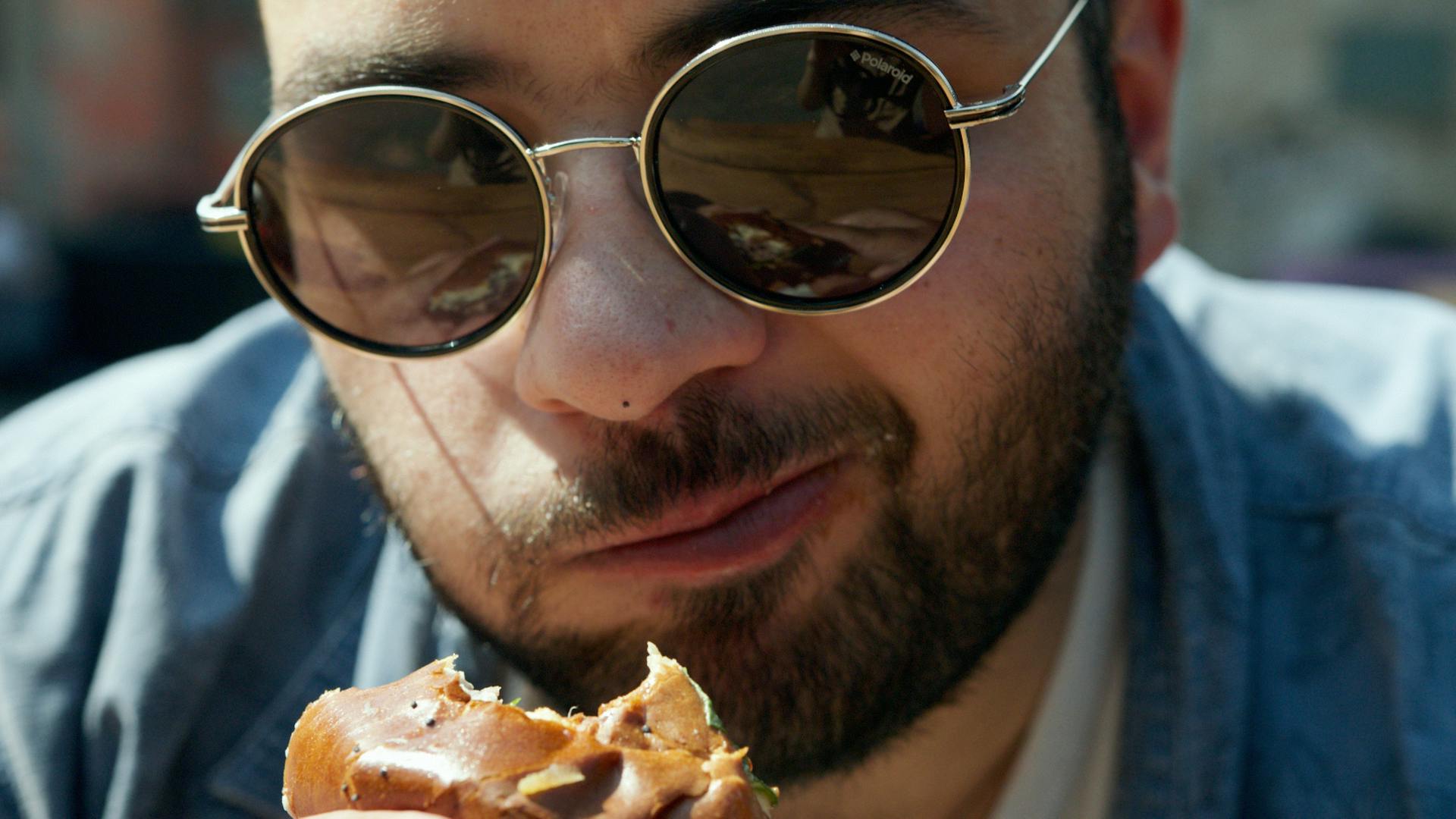 Ein Mann mit schwarz gerahmter Brille isst Pizza | Quelle: Pexels