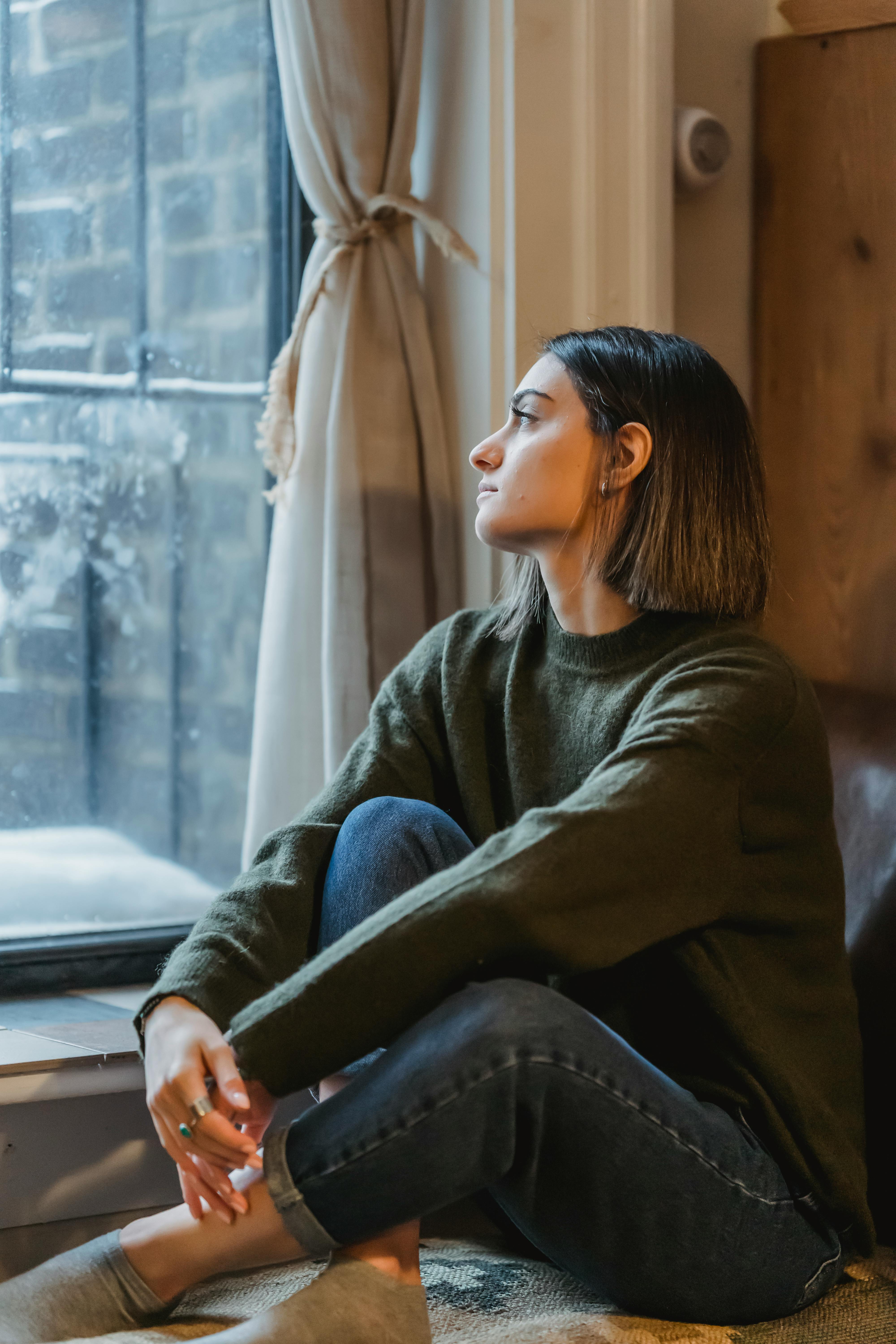 Eine junge Frau schaut nachdenklich aus dem Fenster | Quelle: Pexels