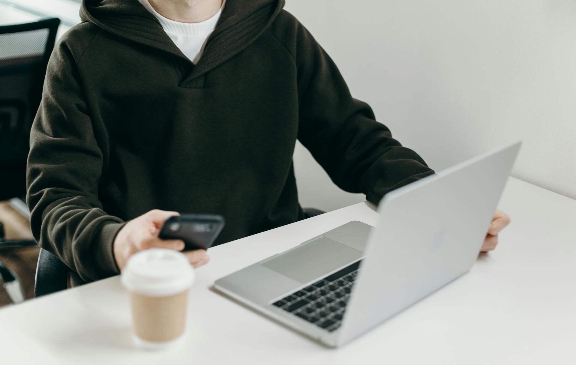 Eine Nahaufnahme eines jungen Mannes, der sein Telefon benutzt, während er an seinem Laptop arbeitet | Quelle: Pexels