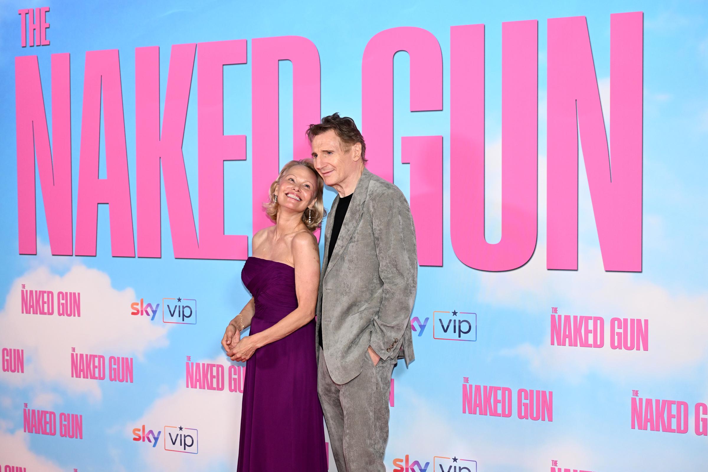 Pamela Anderson lächelt Liam Neeson an, während er ebenfalls in die Kamera lächelt, bei der britischen Premiere von „Die nackte Kanone“ im Cineworld Leicester Square in London, England, am 22. Juli 2025 | Quelle: Getty Images