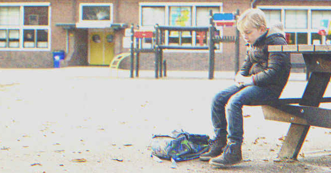Ein Junge sitzt allein auf einer Bank vor einer Schule | Quelle: Shutterstock