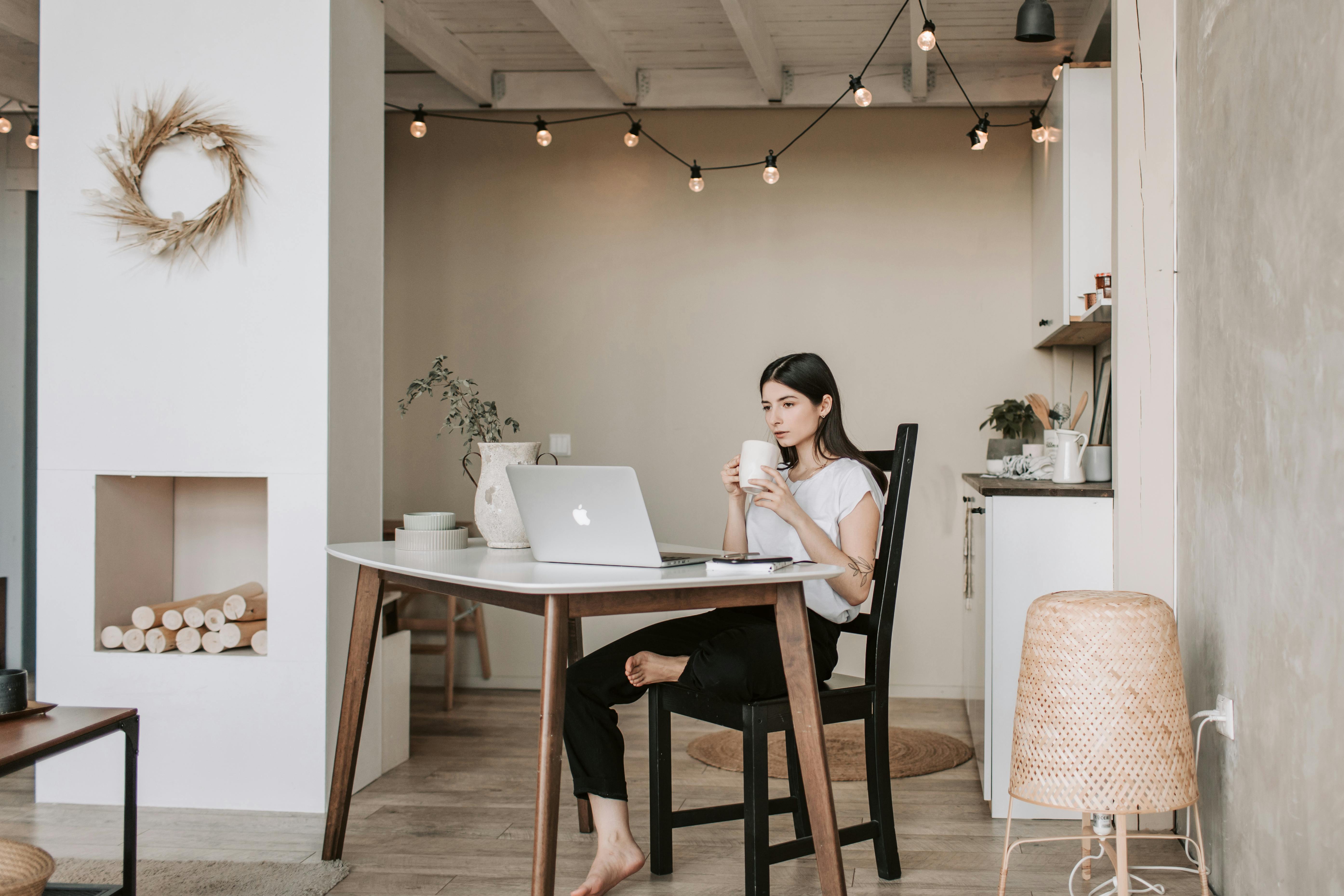 Uma mulher bebe uma bebida enquanto olha algo em seu laptop | Fonte: Pexels