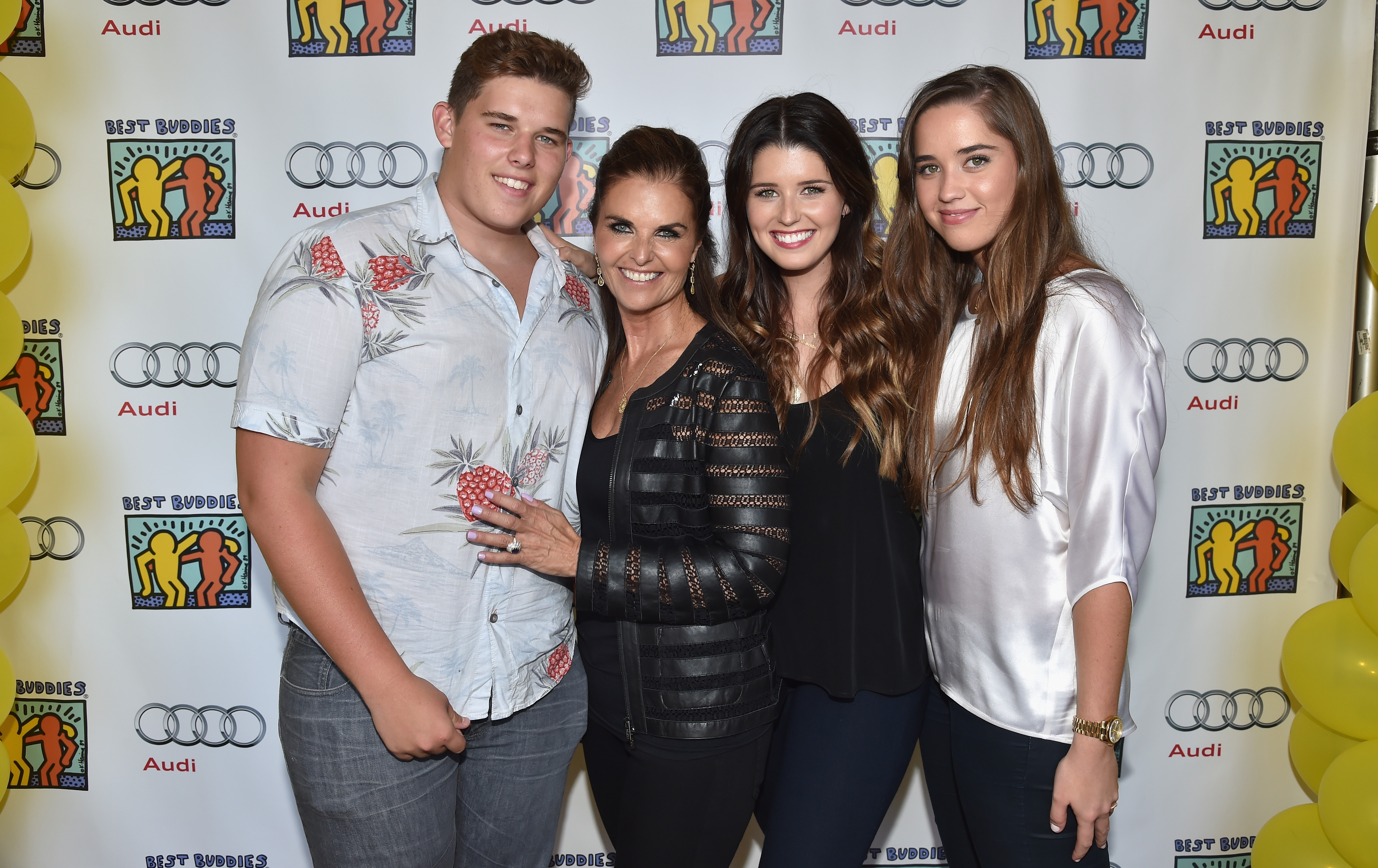 Christopher posiert mit seiner Mutter, Maria Shriver, und seinen Schwestern Katherine und Christina bei einer Veranstaltung in Beverly Hills. Er trägt ein helles Button-Down-Hemd mit einem auffälligen Fruchtmuster und eine graue Jeans. Er steht selbstbewusst da und lächelt, sein kurzes Haar ist ordentlich gestylt und seine Statur ist sichtlich fülliger als früher.