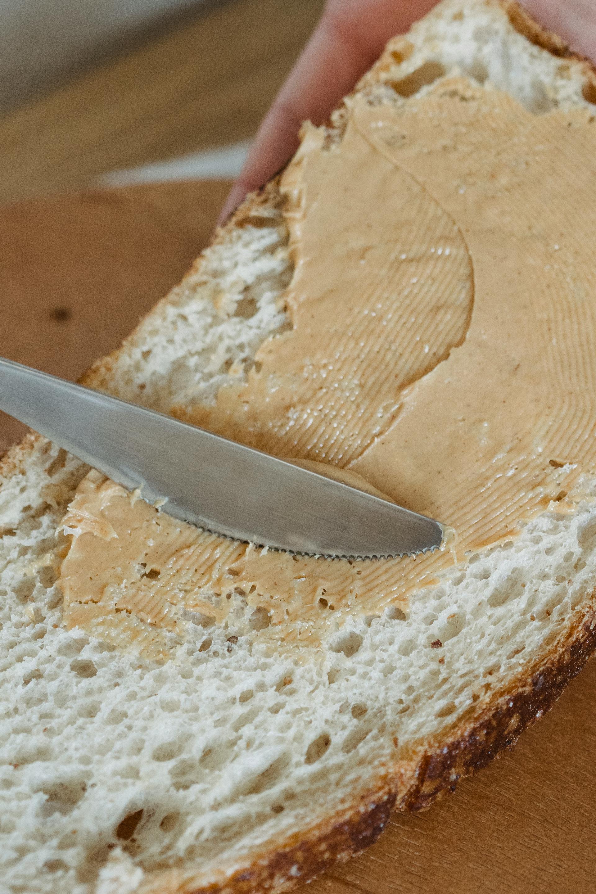 Eine Person schmiert Erdnussbutter auf eine Scheibe Brot | Quelle: Pexels
