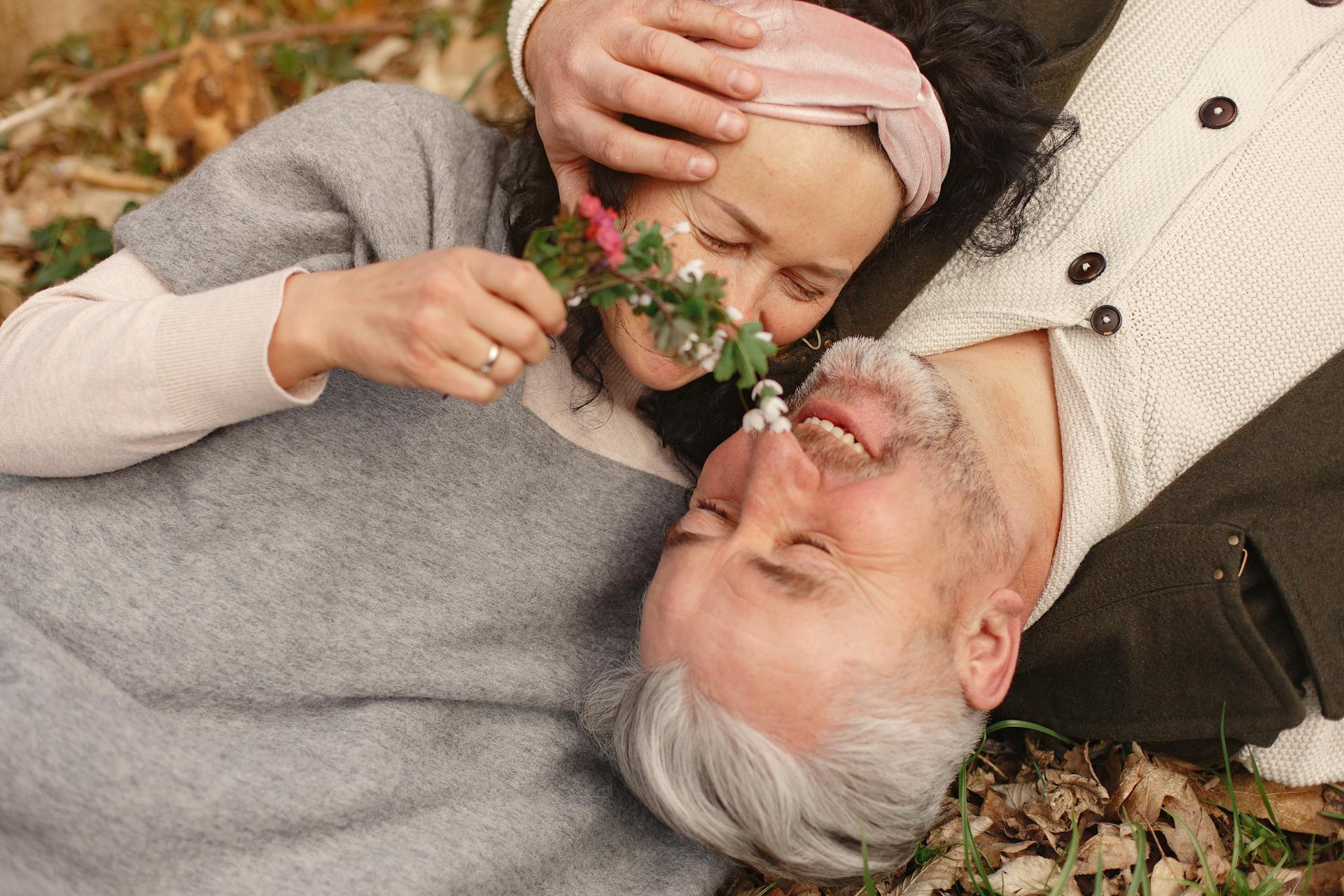 Ein älteres Paar kuschelt, während es sich auf einen Haufen gefallener Blätter legt | Quelle: Pexels