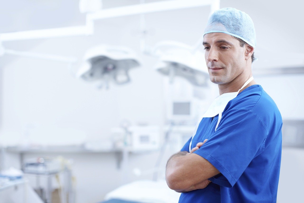 Ein Arzt in blauem Kittel mit gefalteten Händen in einem Krankenhaus | Quelle: Pixabay/Free-Photos
