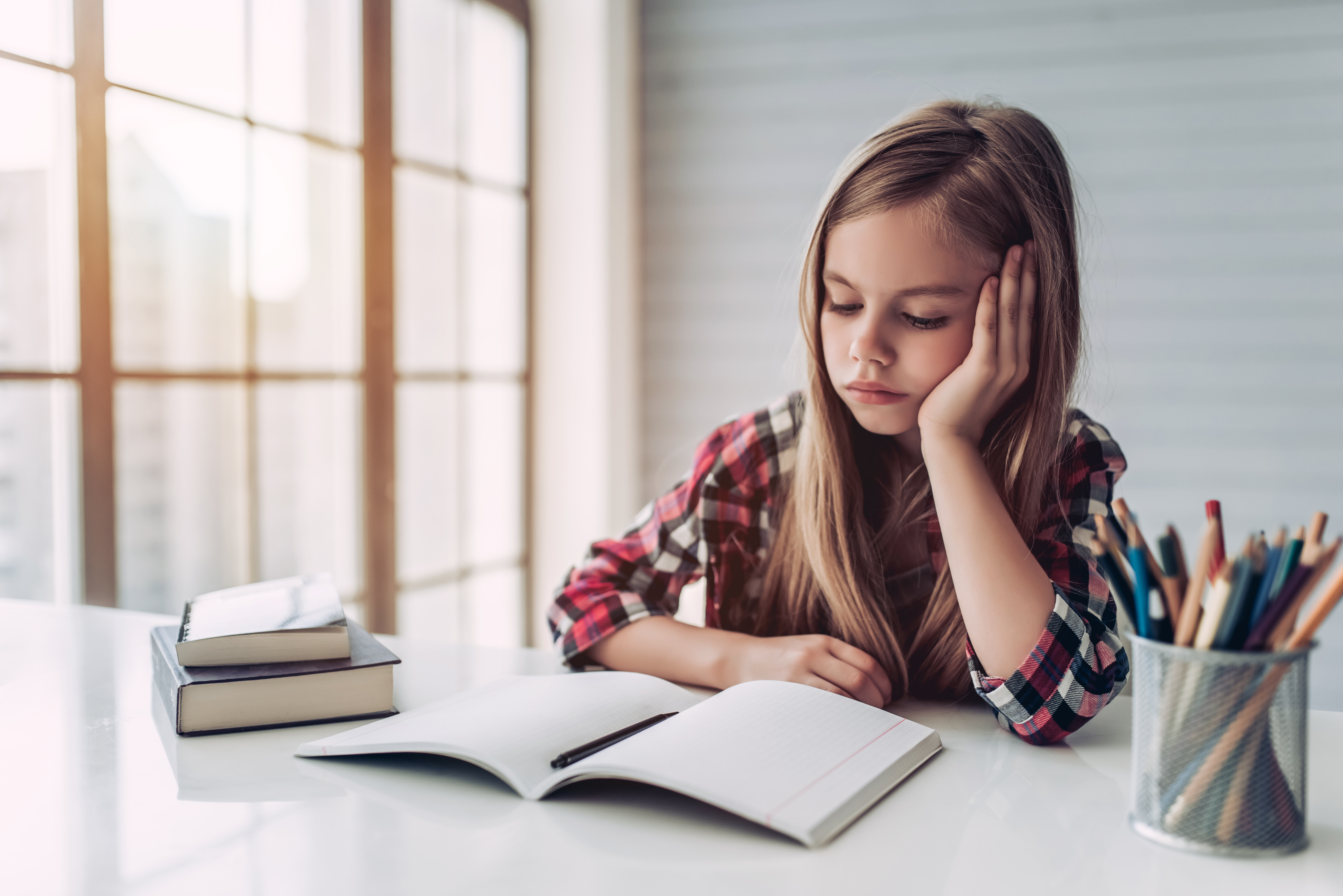 Ein junges, trauriges Mädchen starrt auf ein Buch auf ihrem Schreibtisch | Quelle: Shutterstock