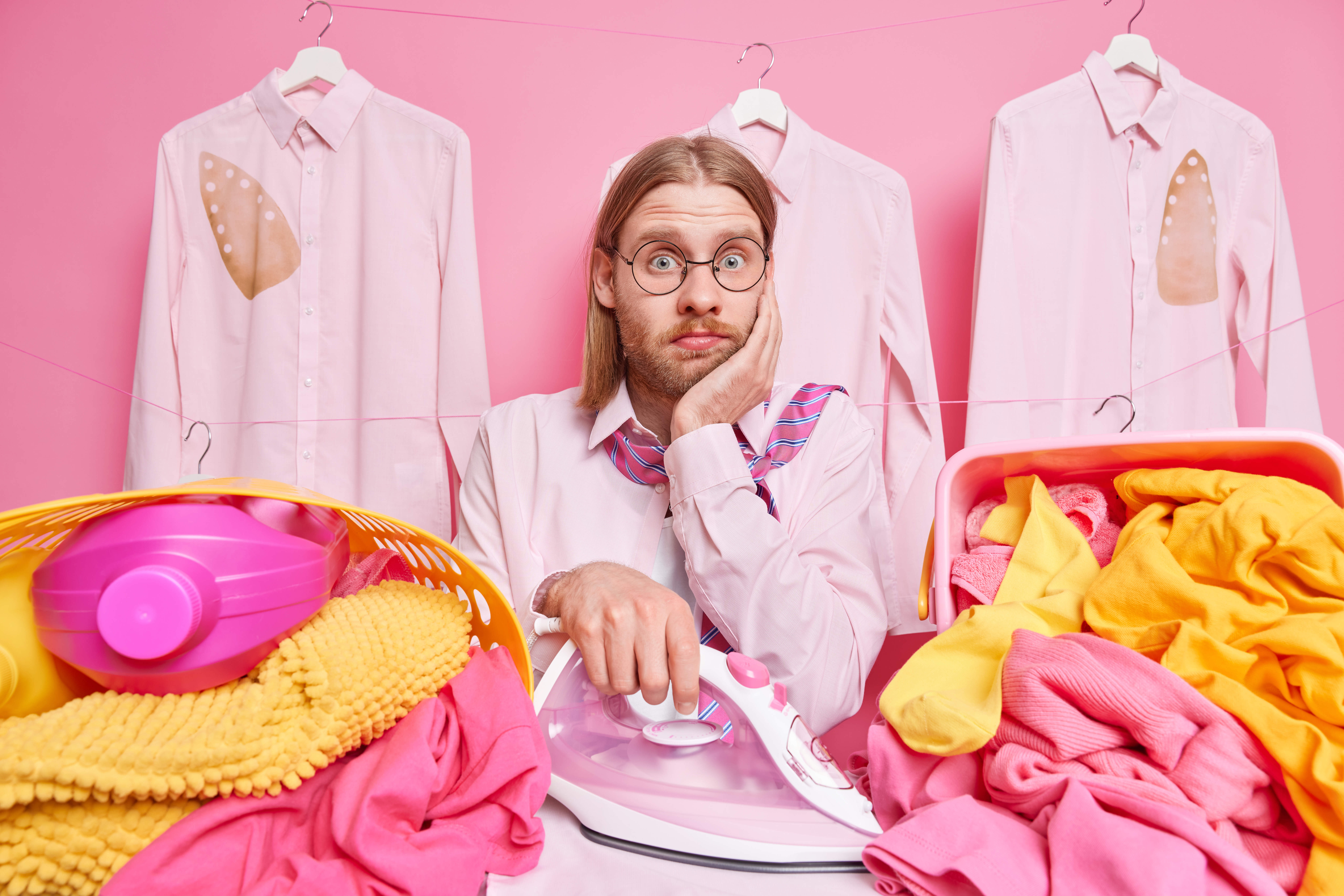 Mann hält ein Bügeleisen inmitten von rosa und gelber Wäsche | Quelle: wayhomestudio auf Freepik