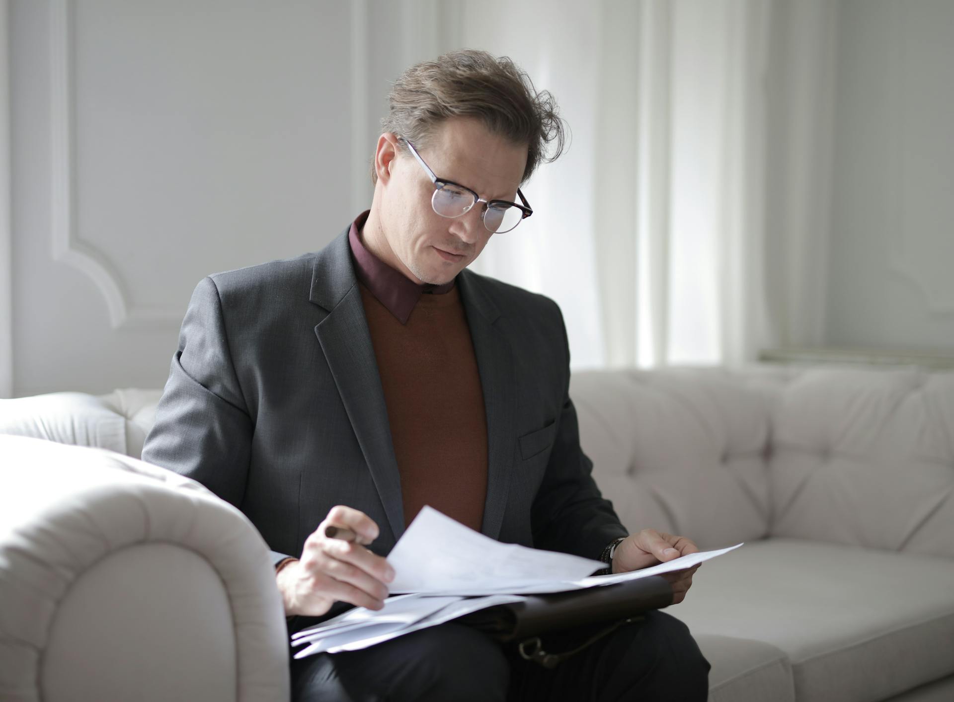 Ein Mann geht wichtige Dokumente durch, während er auf einer Couch sitzt | Quelle: Pexels