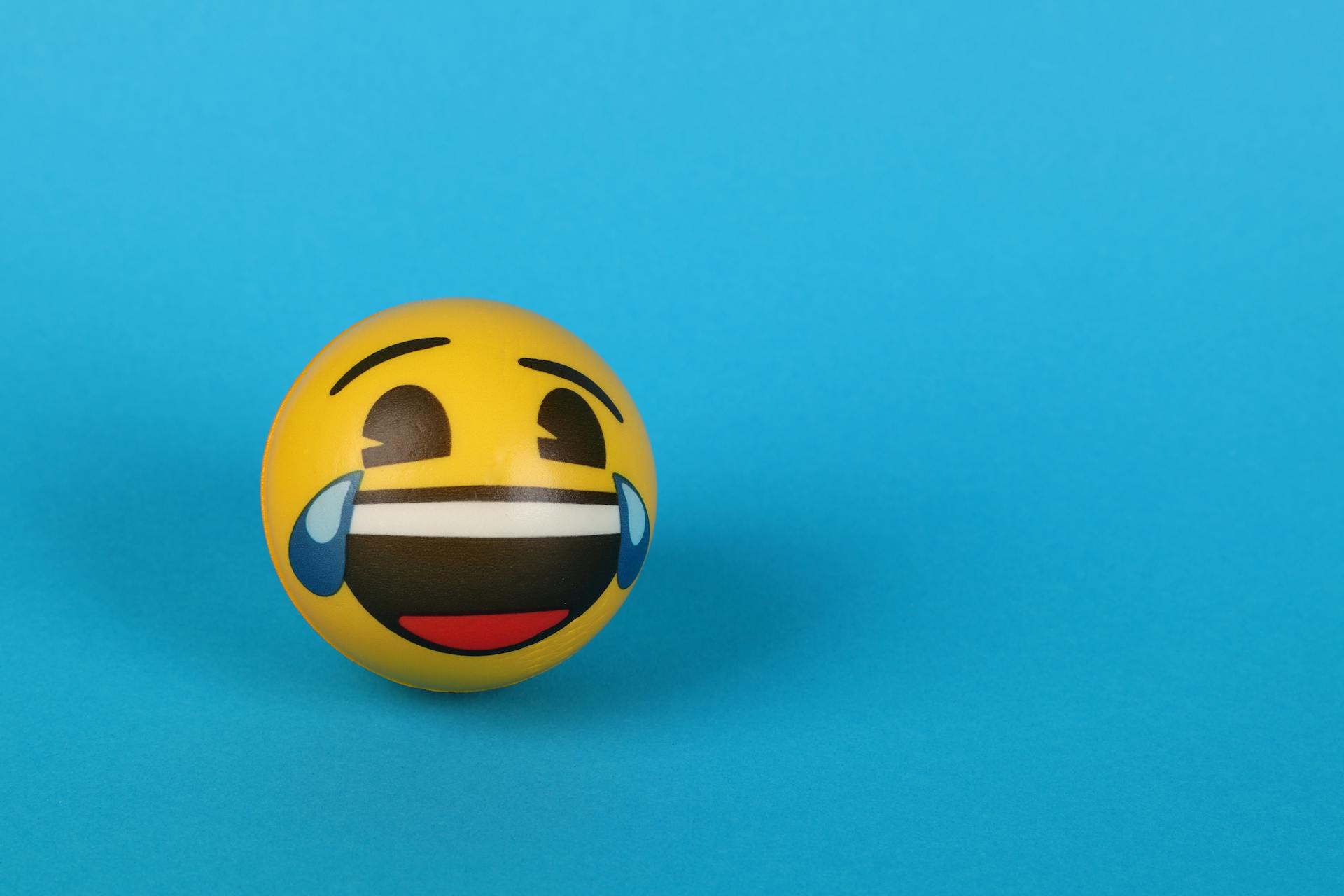 Ein lachendes Emoji mit Tränen über einer blauen Fläche | Quelle: Pexels