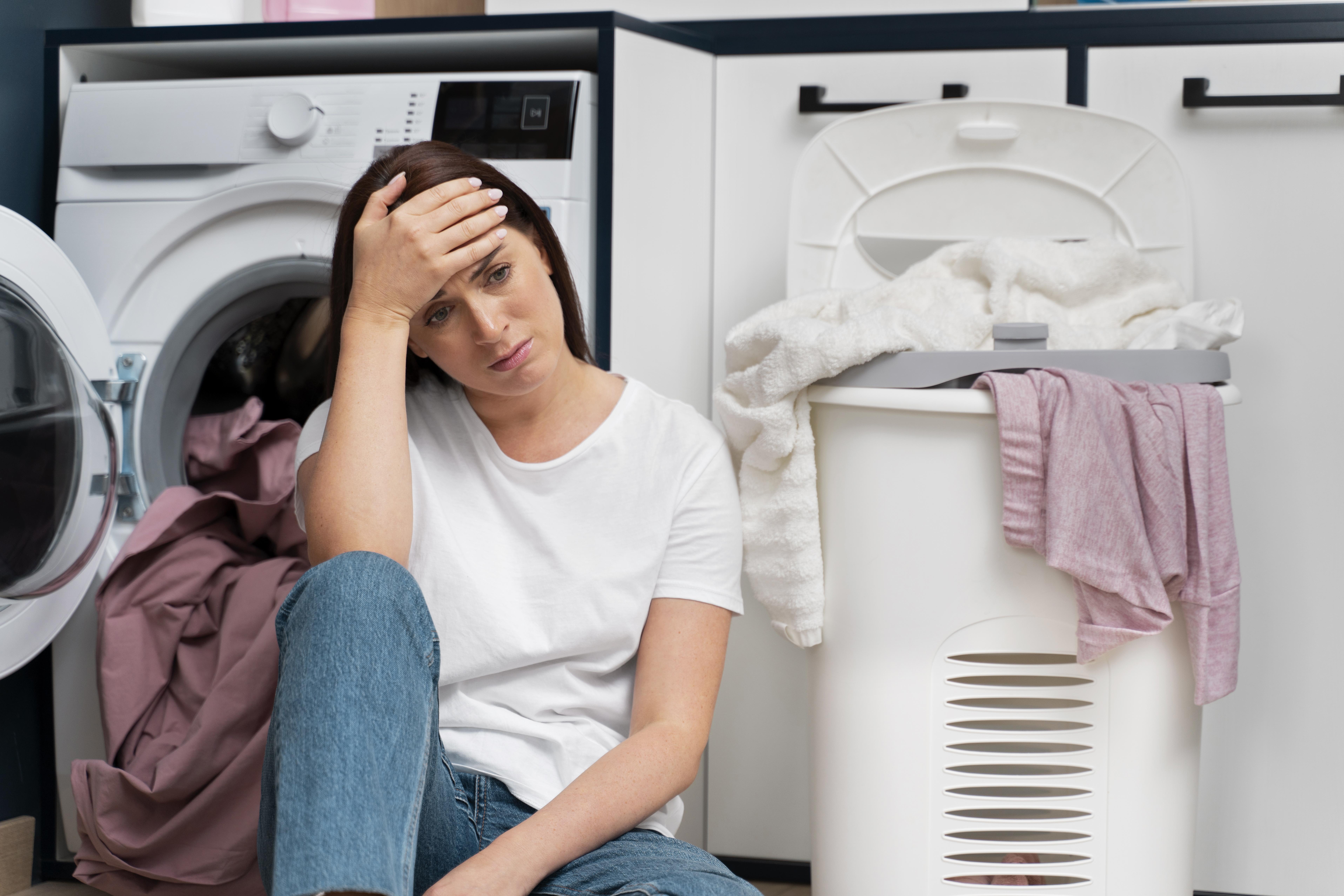 Eine Frau lehnt sich verärgert an eine Waschmaschine, umgeben von Wäsche | Quelle: Freepik