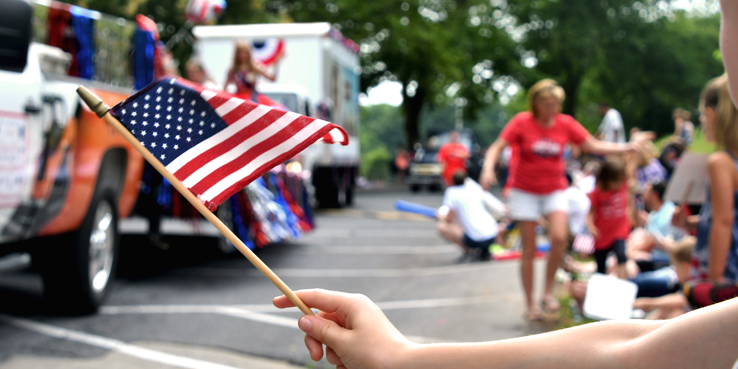 Eine Person schwenkt eine amerikanische Flagge während einer lebhaften Parade zum 4. Juli | Quelle: Shutterstock