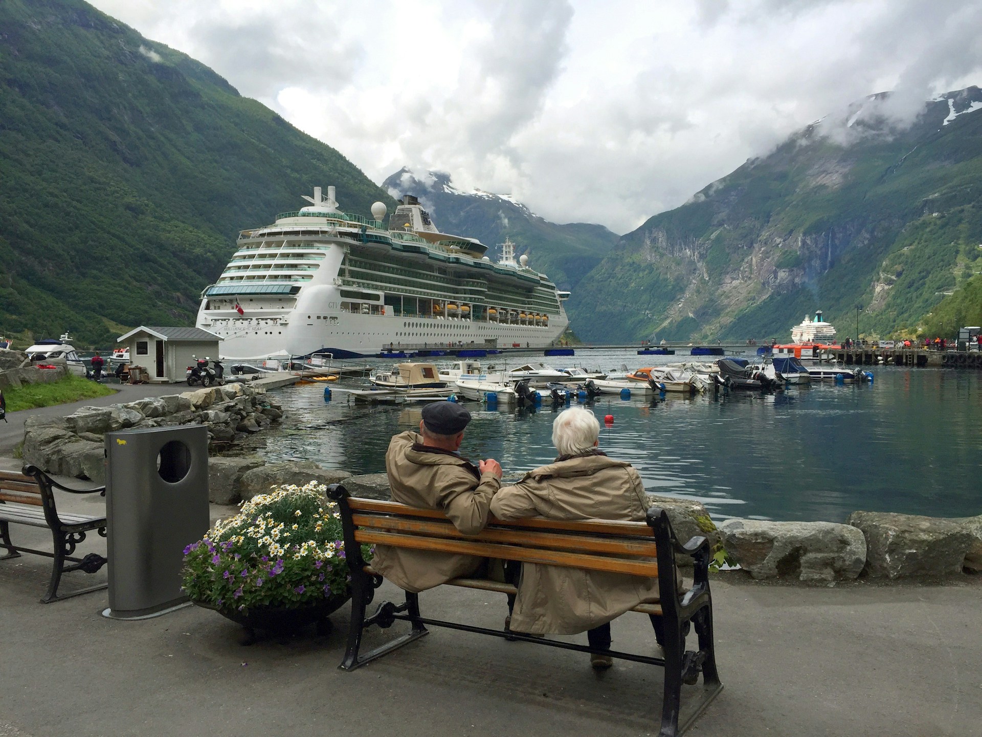 Ein älteres Paar sitzt auf einer Bank und beobachtet ein Kreuzfahrtschiff | Quelle: Unsplash