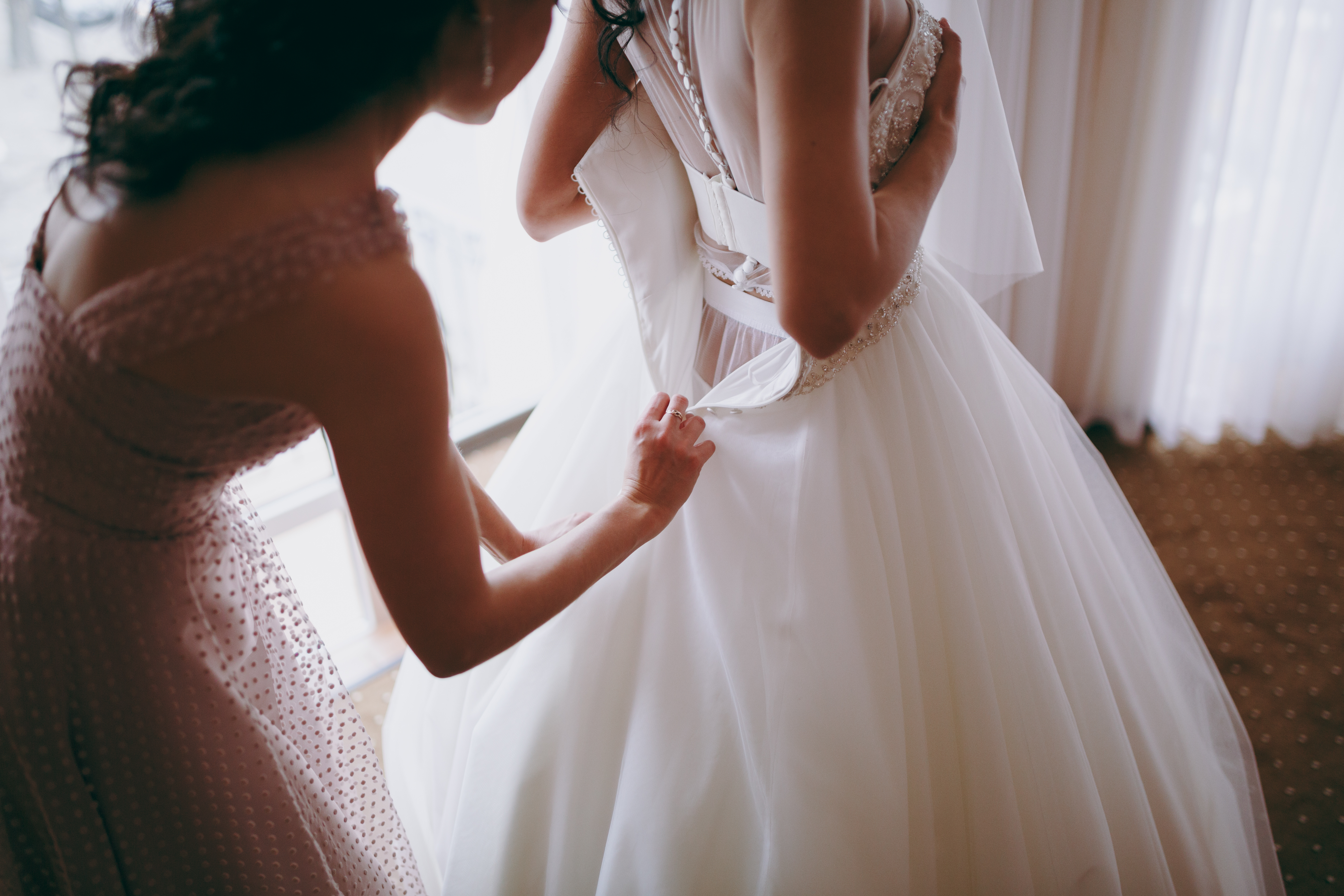 Eine Frau hilft einer Braut beim Anziehen ihres Brautkleides | Quelle: Shutterstock