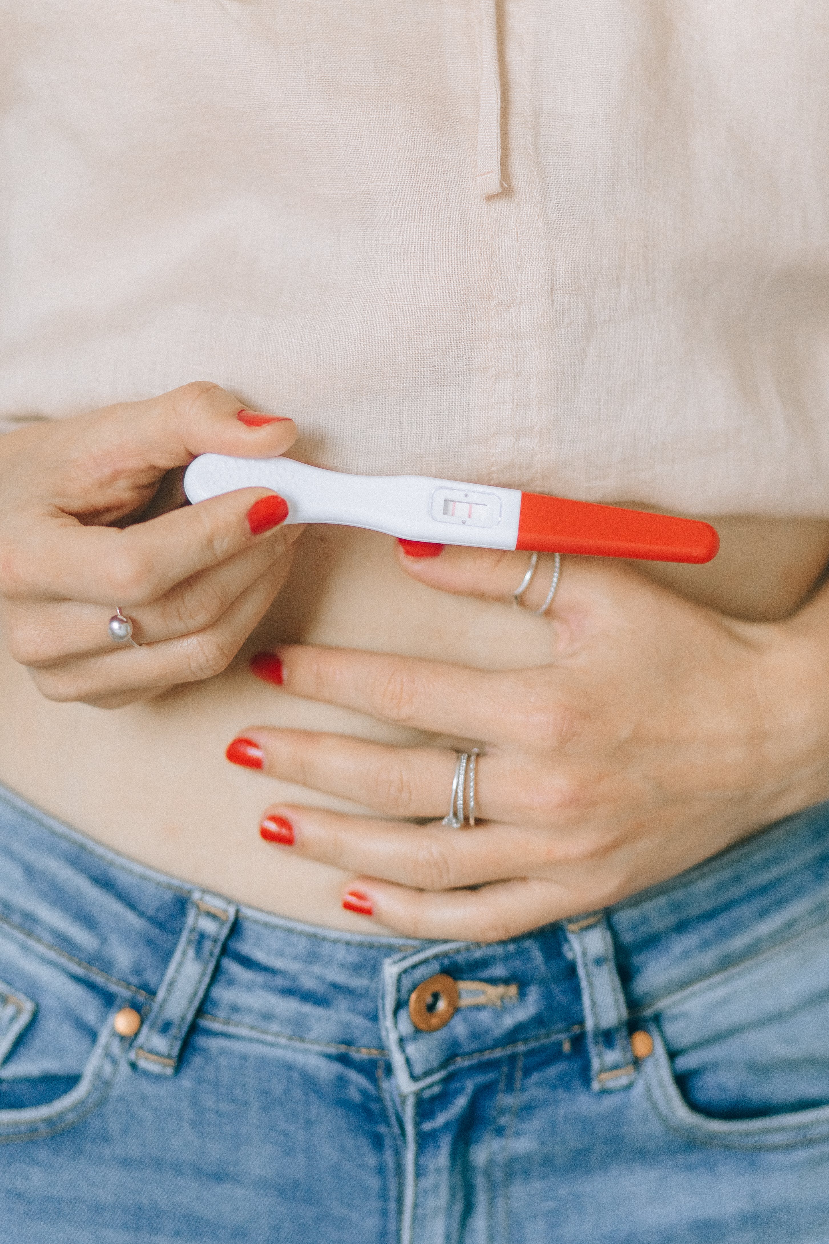Eine Frau, die ihren Bauch und einen Schwangerschaftstest hält | Quelle: Pexels