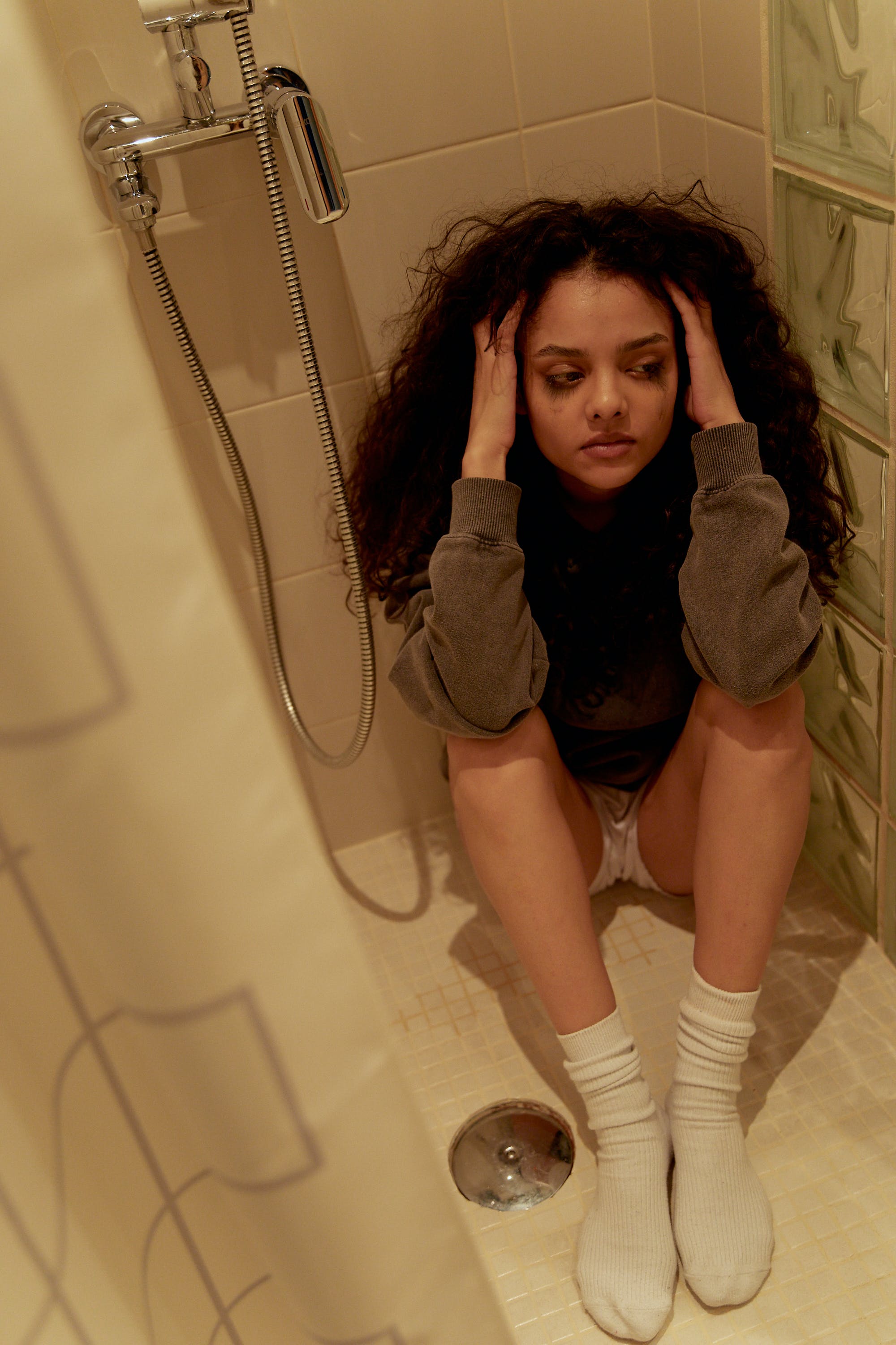 Eine aufgebrachte junge Frau, die weinend auf dem Boden einer Dusche sitzt | Quelle: Pexels