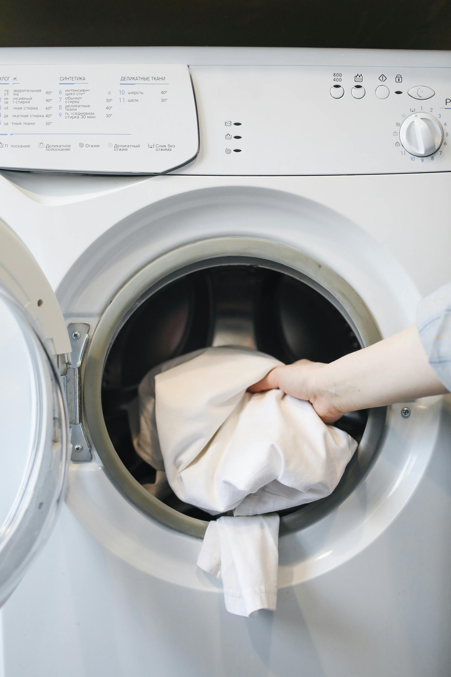 Eine Person, die Kleidung in eine Waschmaschine steckt | Quelle: Pexels