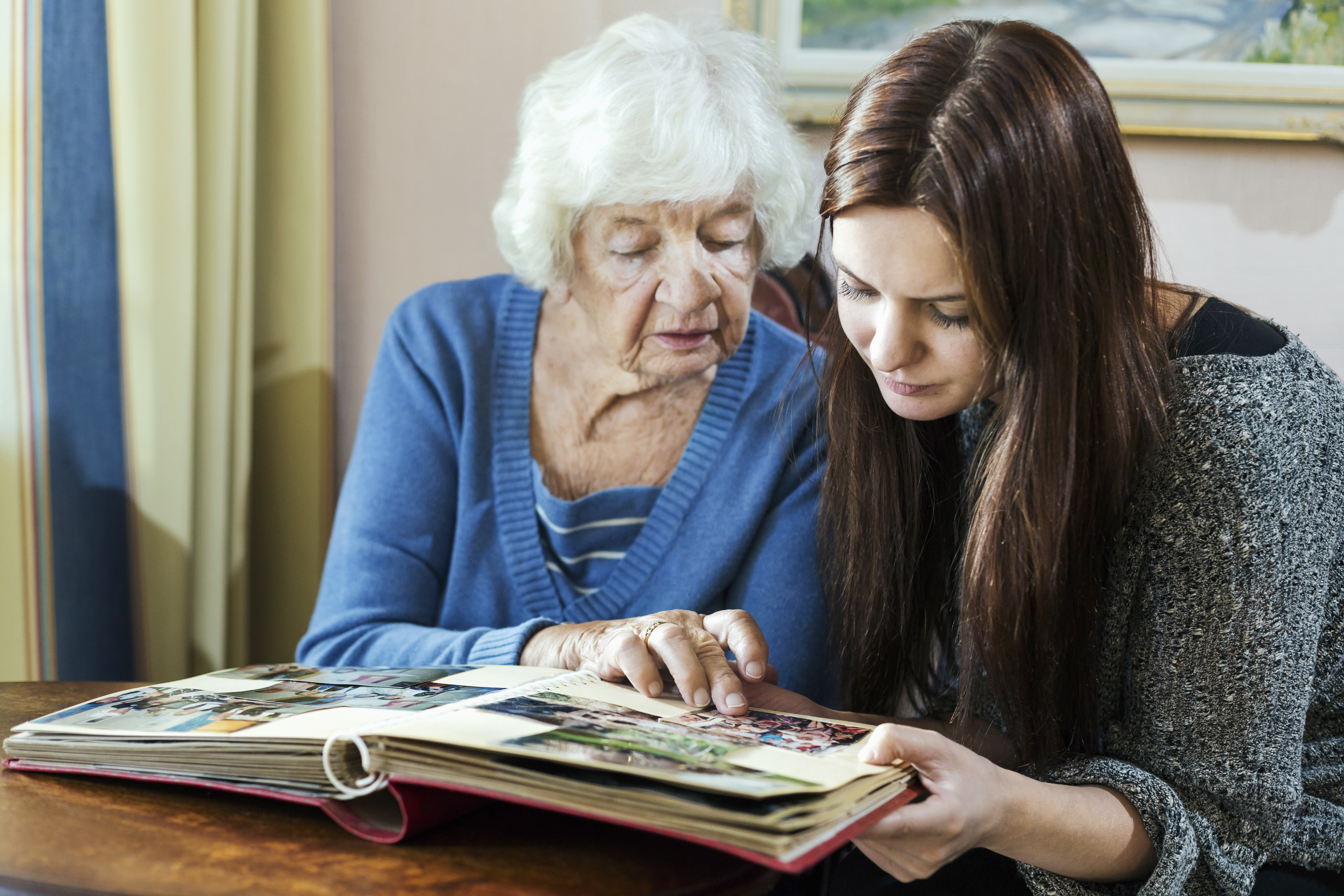 Großmutter und Enkelin betrachten ein Fotoalbum im Haus | Quelle: Getty Images