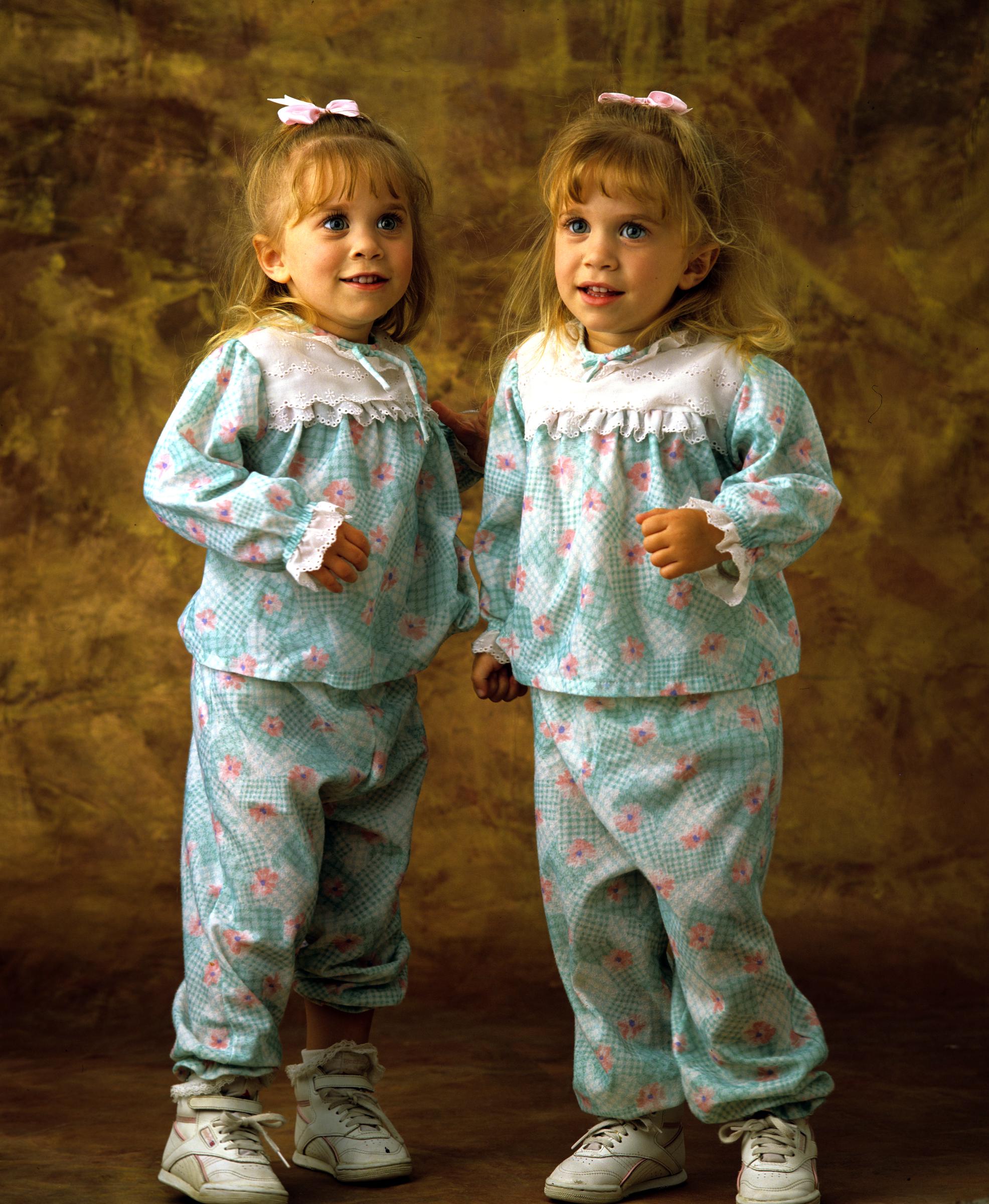 Am 21. September 1990 tauschten die vierjährigen Zwillinge ihren weichen Kleinkind-Blick gegen wache, ausdrucksstarke Kindergesichter, die von einem geraden Pony eingerahmt wurden, und verkörperten den Komfort der frühen 1990er Jahre in aufeinander abgestimmten türkisfarbenen und zartrosa Loungewear-Sets mit Latzchen aus Lochspitze, gerüschten Bündchen und weißen High-Top-Sneakern.