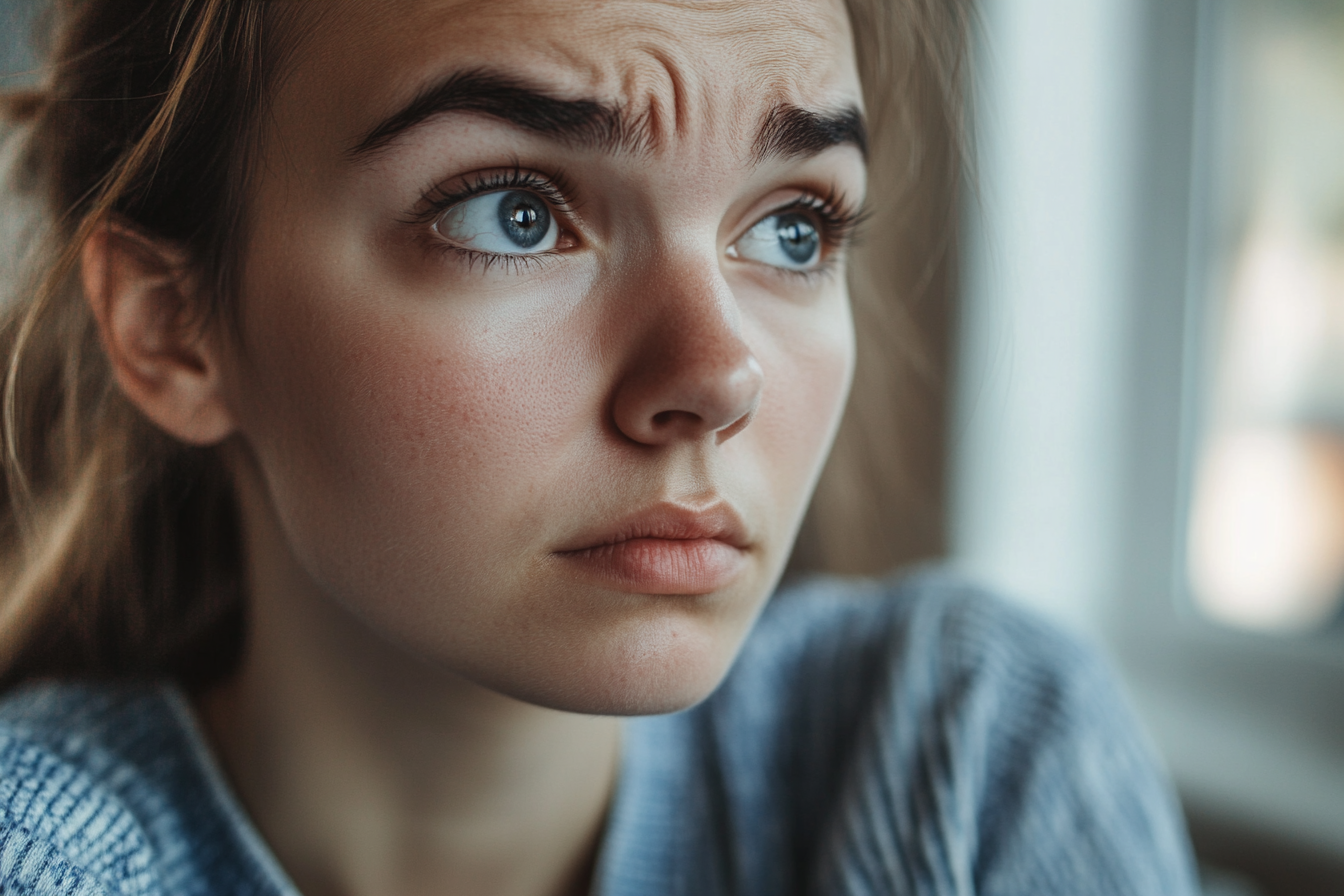 Eine Frau runzelt die Stirn, während sie in Gedanken versunken ist | Quelle: Midjourney