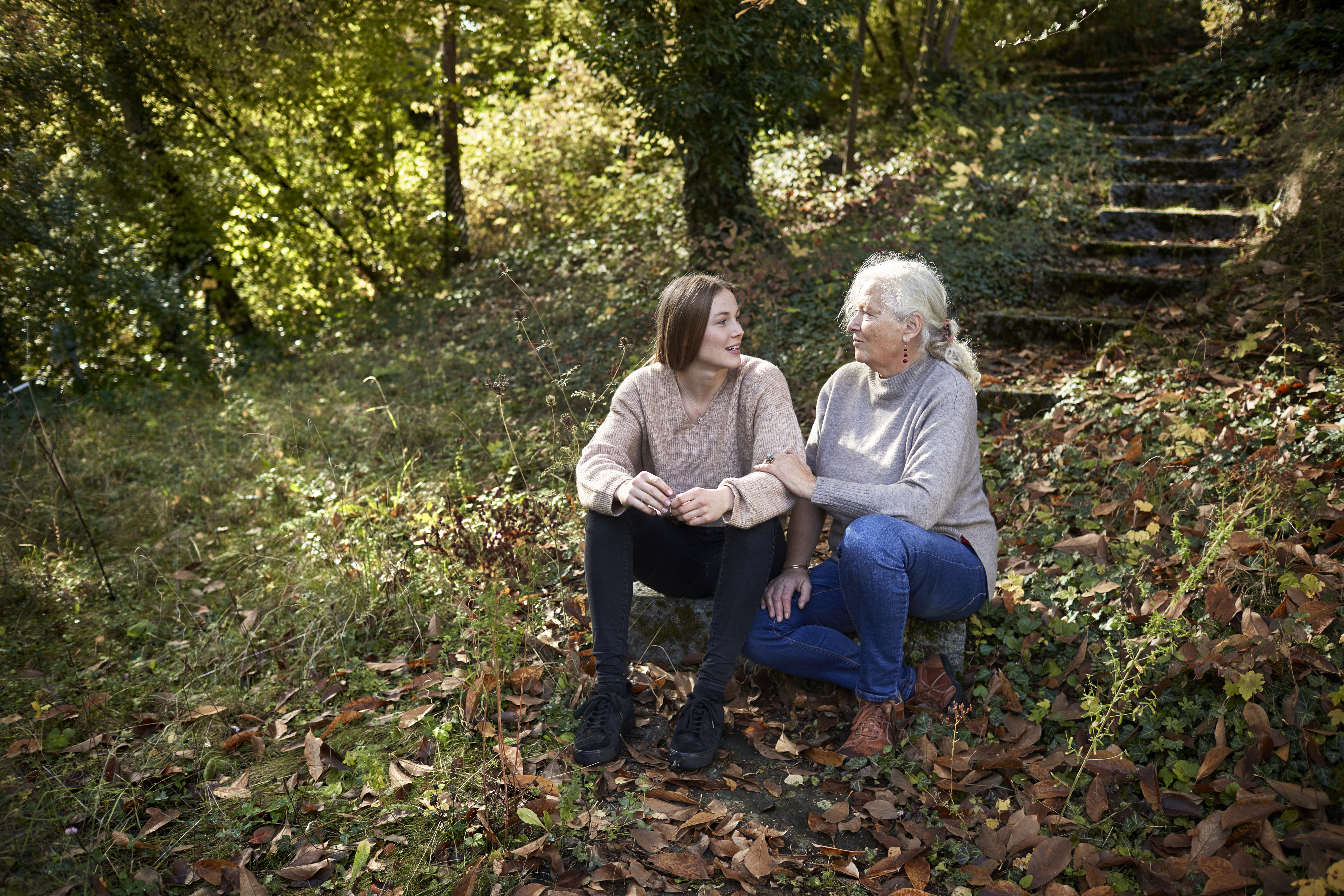 Großmutter und erwachsene Enkelin sitzen im herbstlichen Garten | Quelle: Getty Images