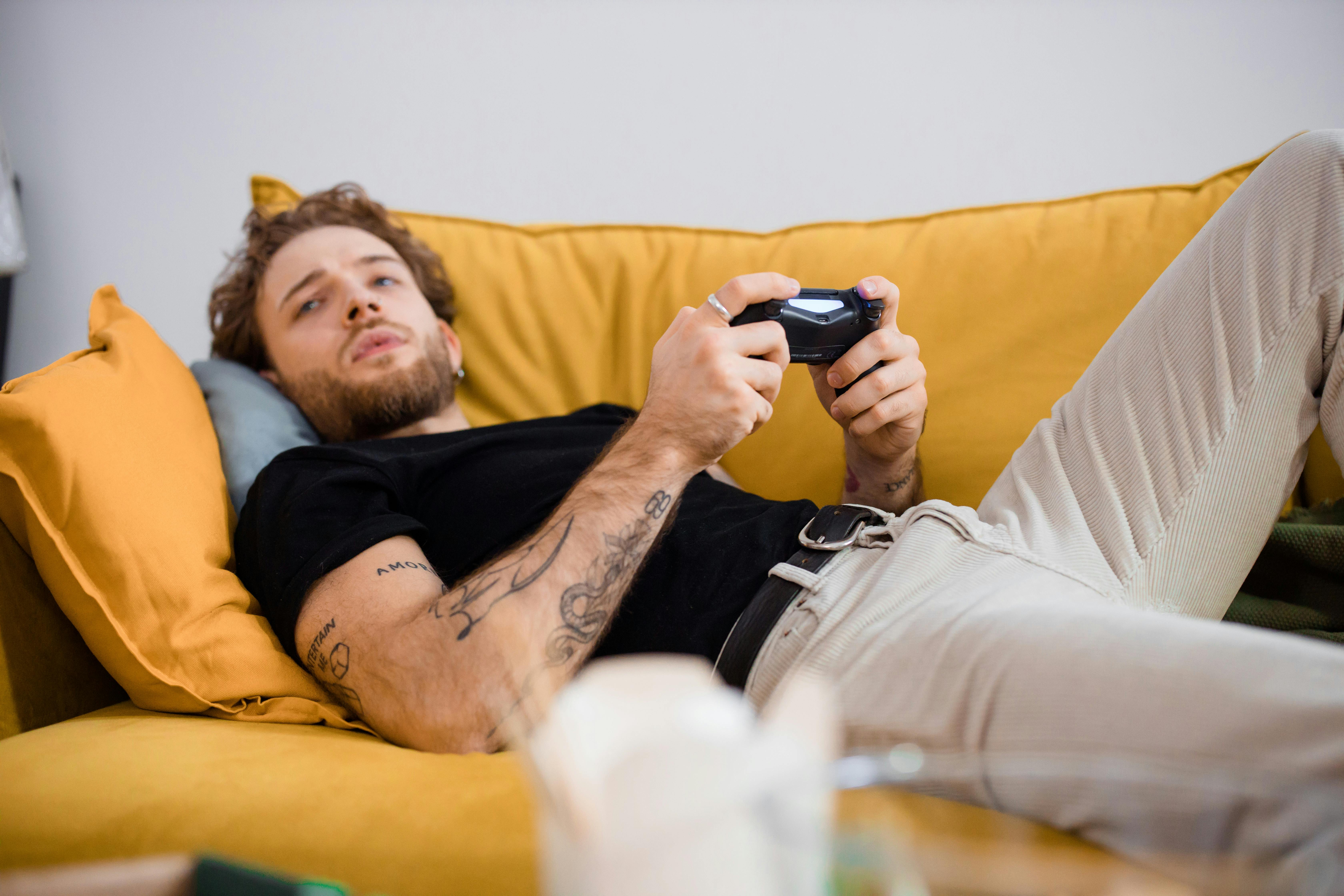 Ein Mann spielt ein Fernsehspiel, während er auf einer Couch liegt | Quelle: Pexels