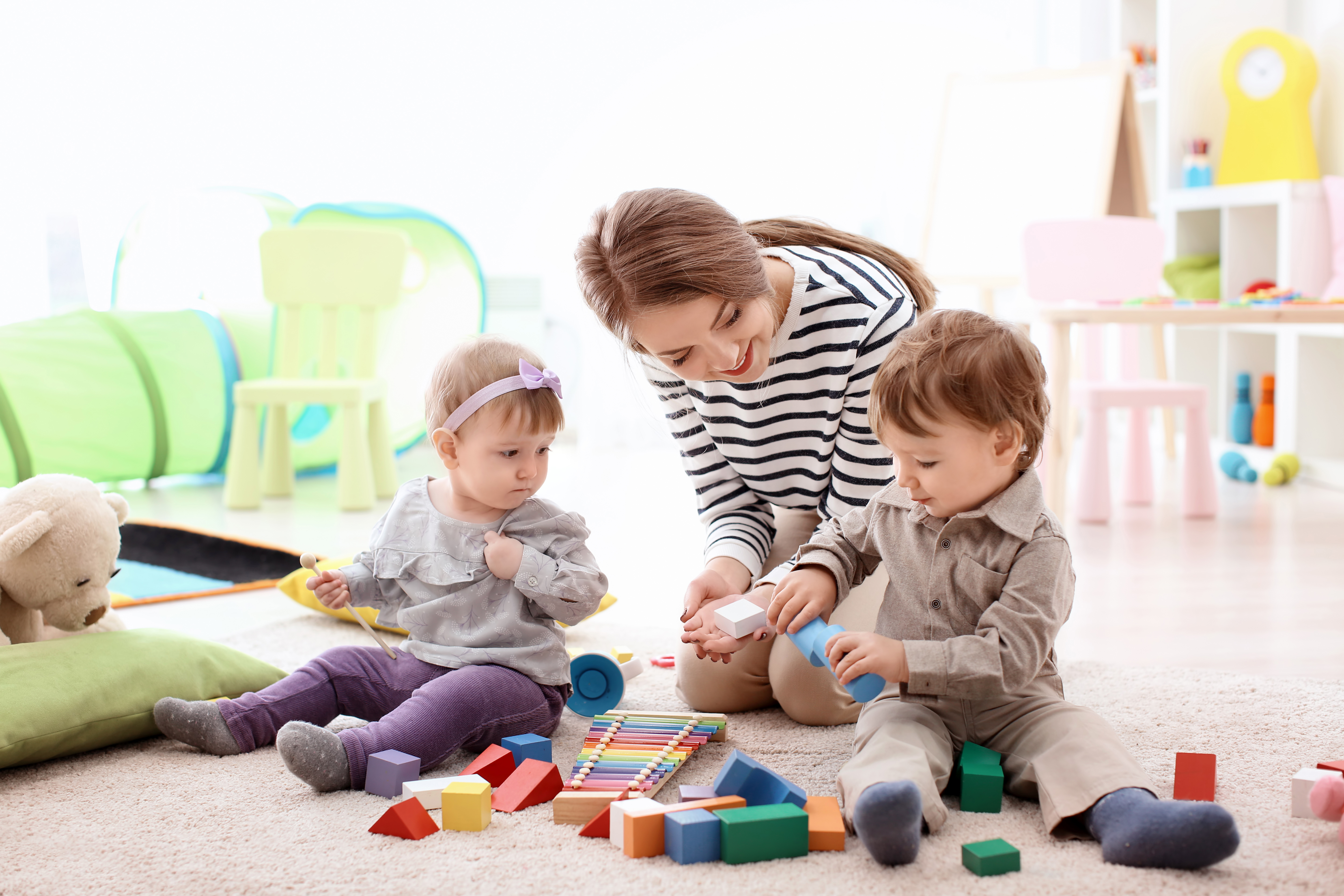 Eine junge Frau, die zwei Kleinkindern beim Spielen hilft | Quelle: Shutterstock