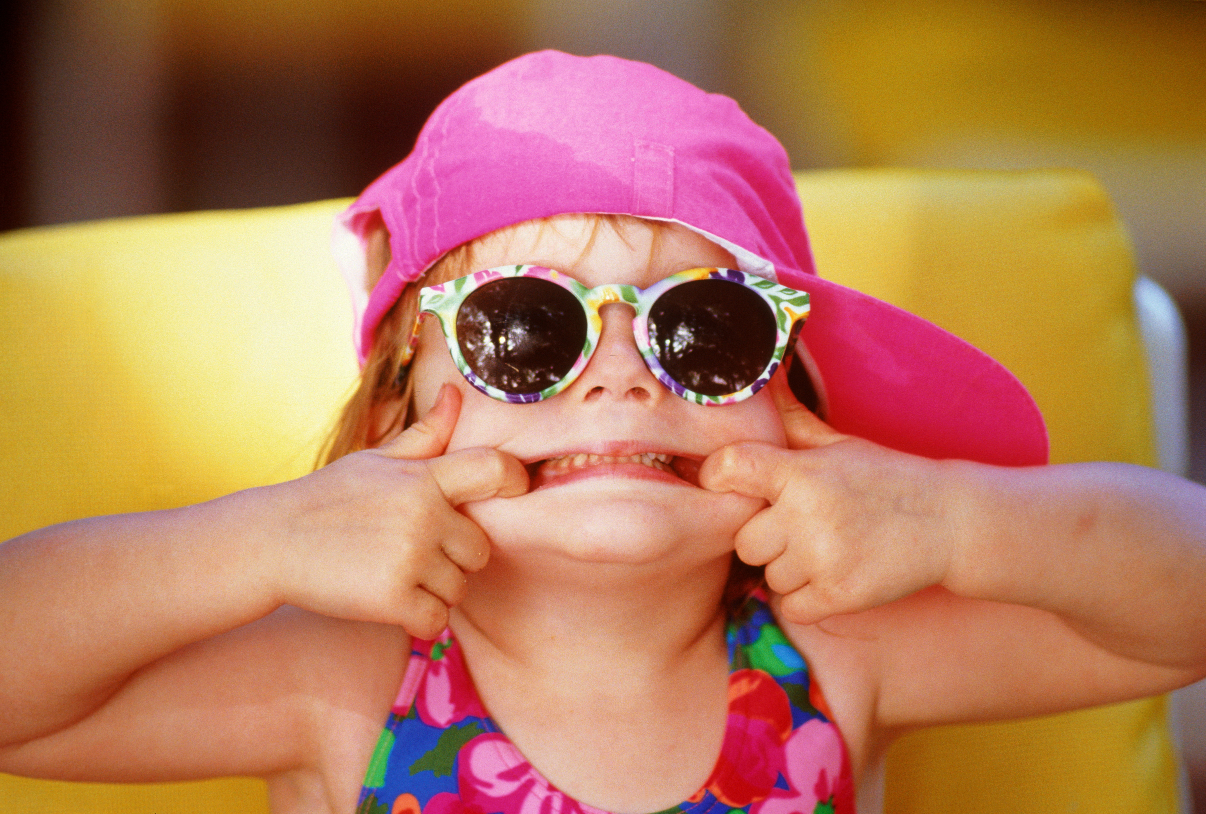 Mädchen (2-4) im Badeanzug, Mütze und Sonnenbrille, Gesicht verziehend, Nahaufnahme | Quelle: Getty Images
