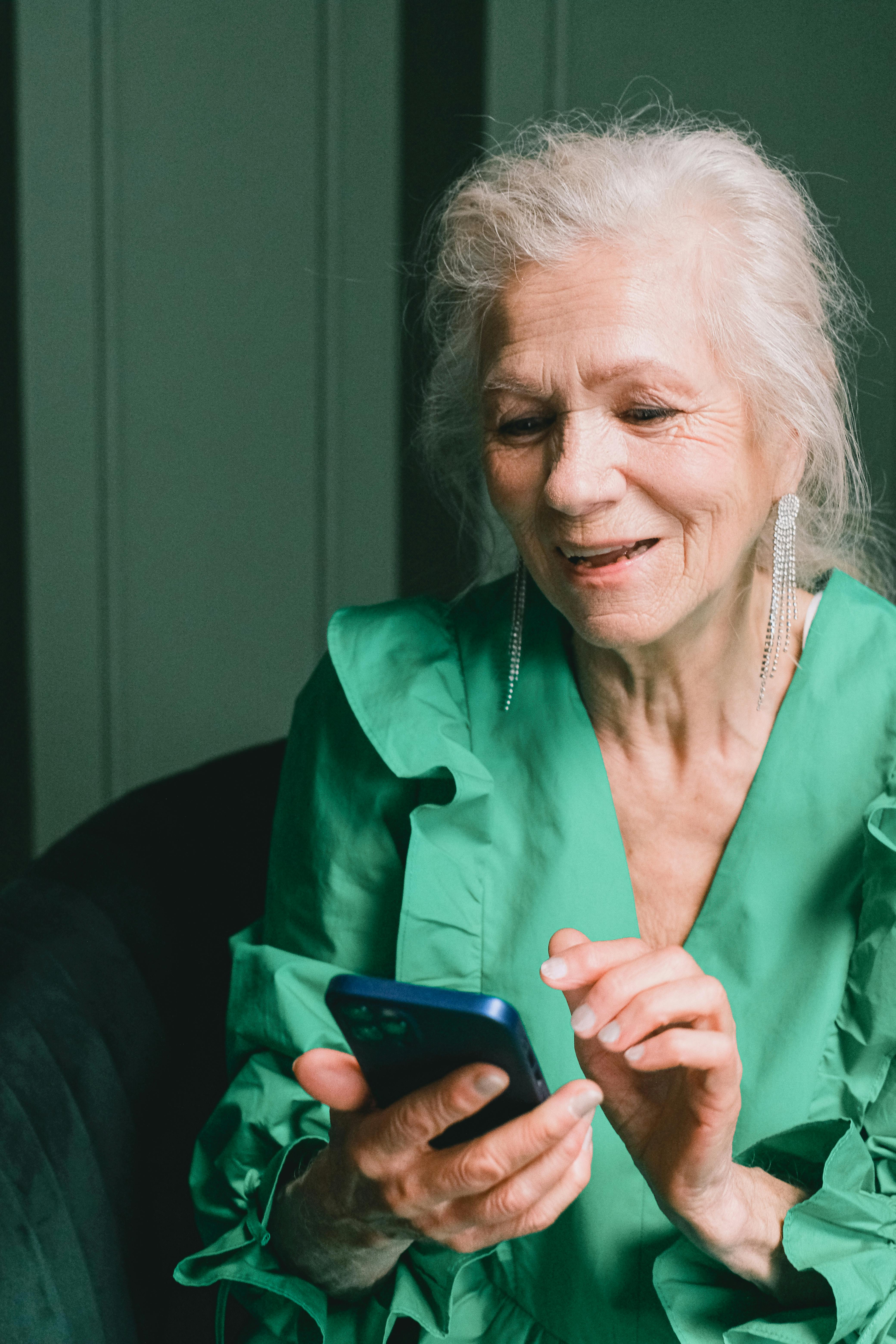 Eine ältere Frau, die lächelt, während sie ein Telefon benutzt | Quelle: Pexels