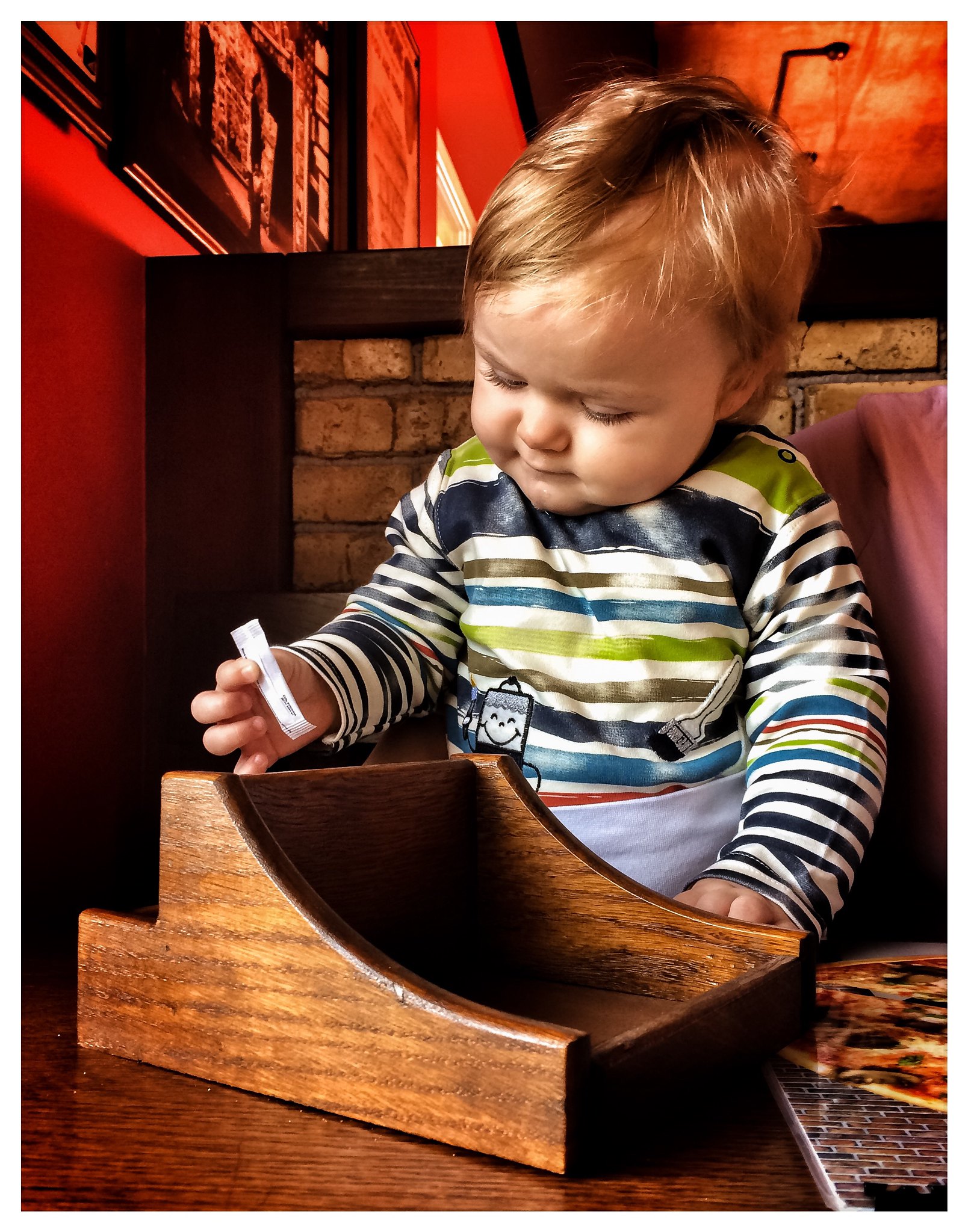 Ein kleiner Junge spielt mit einem Zuckertütchen in einem Restaurant | Quelle: Flickr